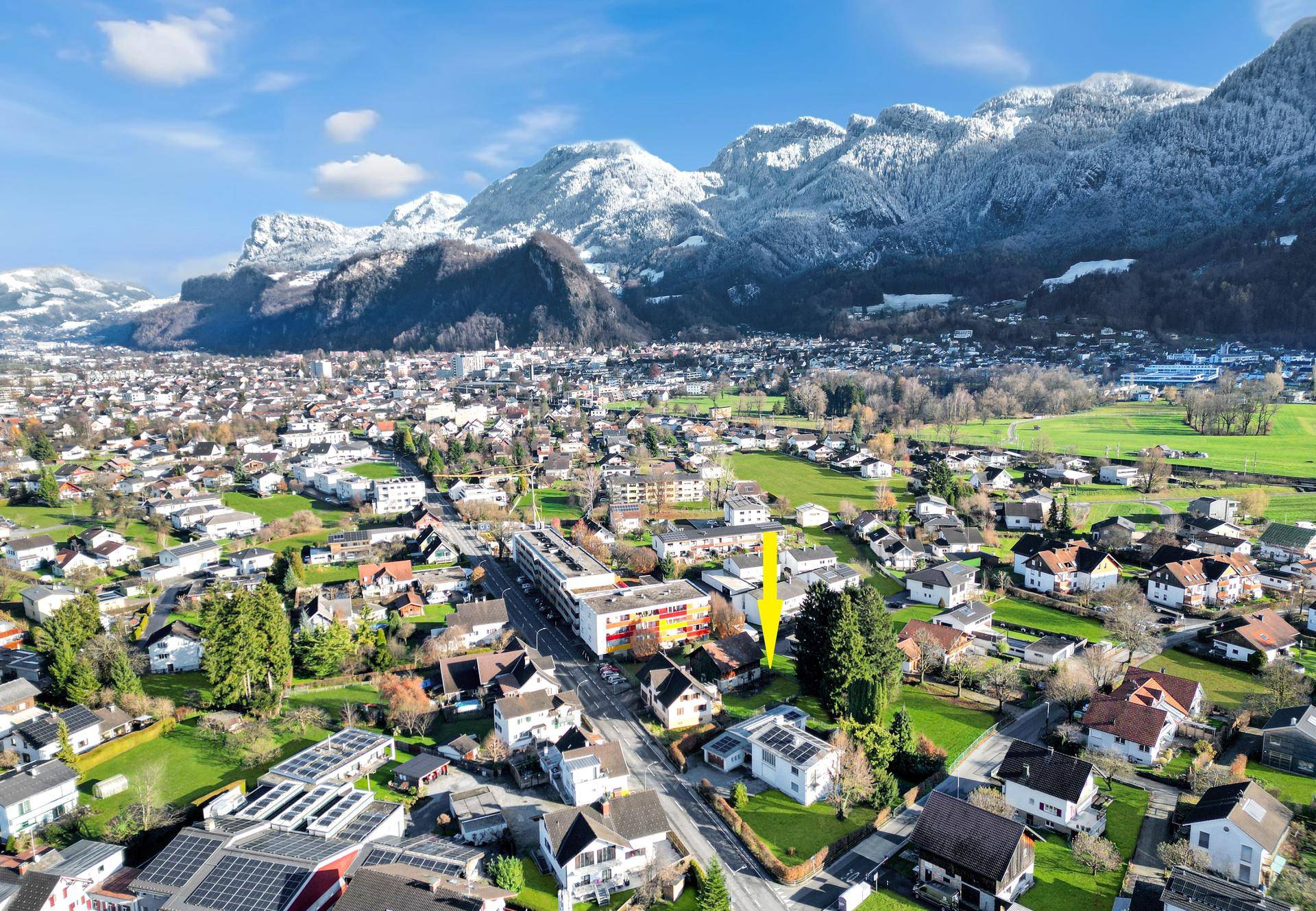 Weitläufige Luftaufnahme einer Stadt mit schneebedeckten Bergen im Hintergrund, die ein Gebiet hervorhebt.