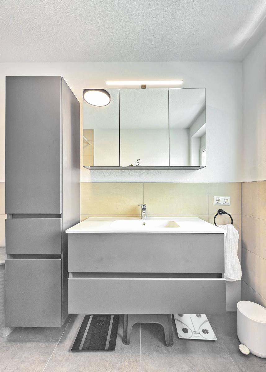 Badezimmer mit modernem Waschtisch, Spiegelschrank und grauen Möbeln.