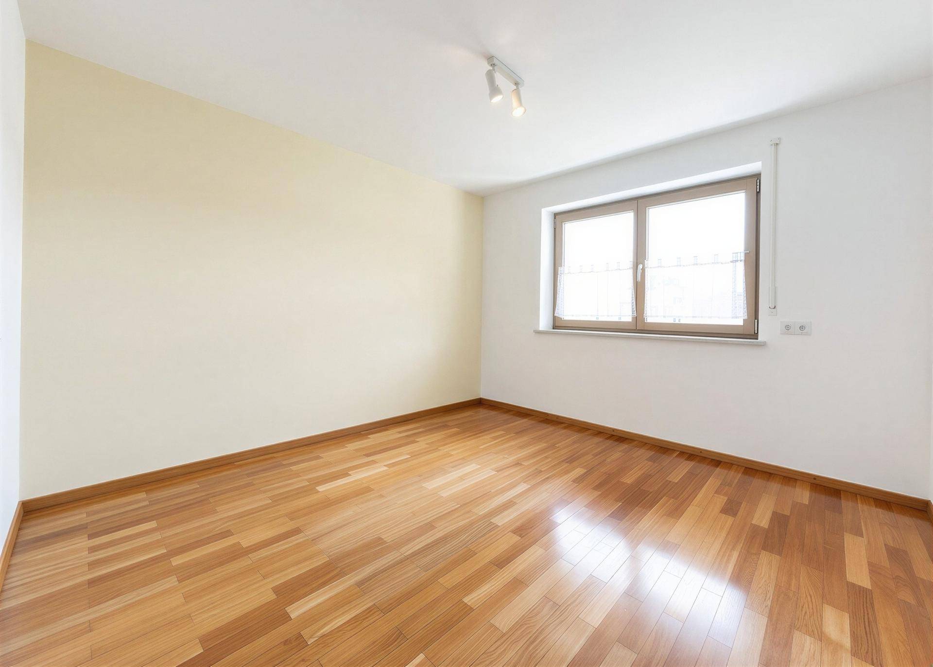 Leeres Zimmer mit Holzboden und einem Fenster, bereit zur individuellen Gestaltung.