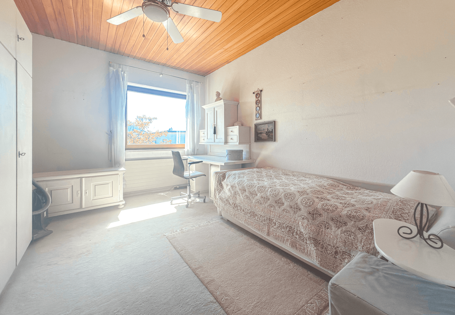 Helles Schlafzimmer mit Holzdecke, Schreibtisch und Blick nach draußen.