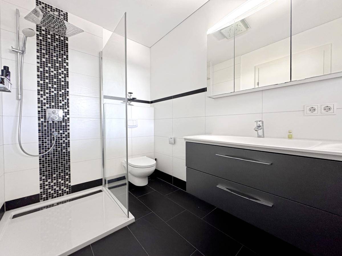 Elegantes Badezimmer mit moderner Dusche, Waschtisch und dunklen Bodenfliesen.