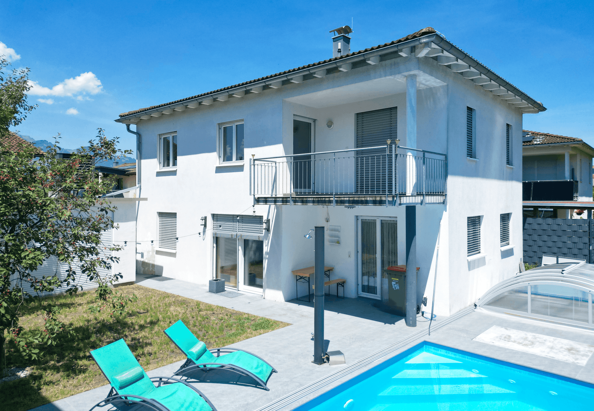 Ansicht des Hauses mit Pool, Liegewiese und Balkon unter blauem Himmel.