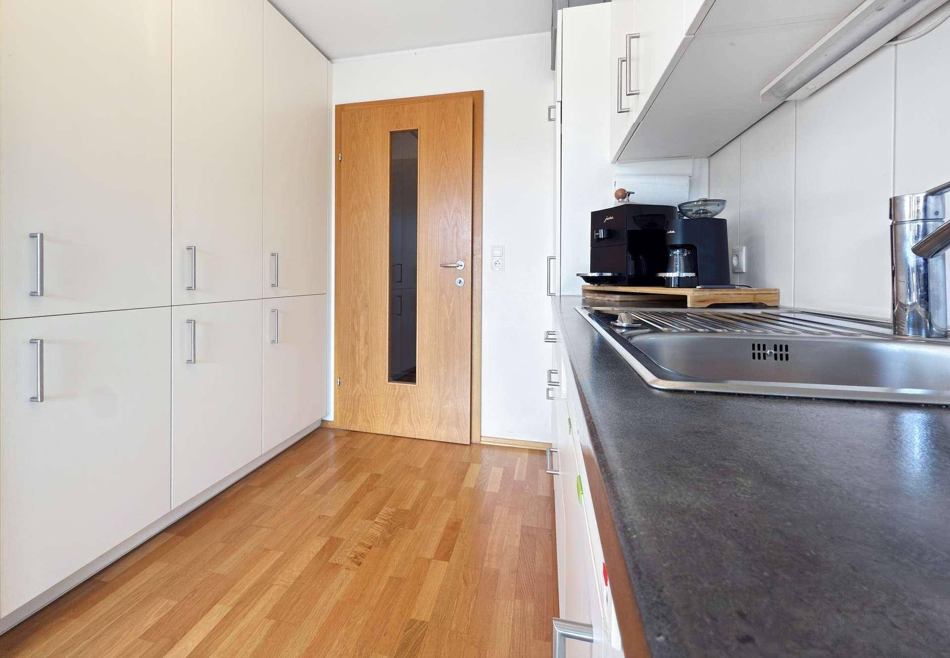 Helle Küche mit weißen Schränken, dunkler Arbeitsplatte und Holzboden.