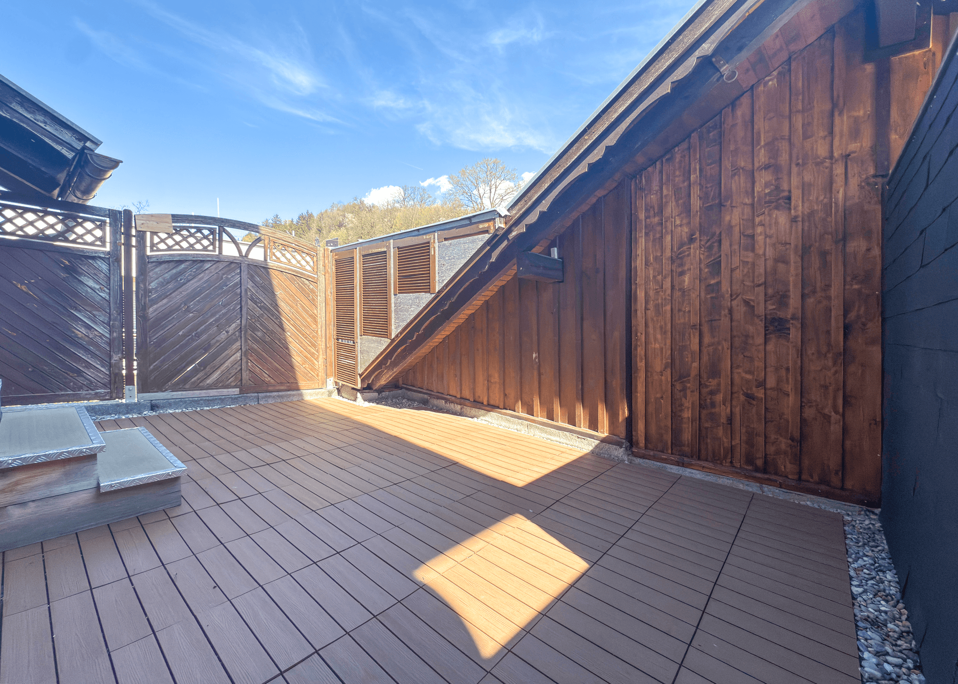 Sonnige Dachterrasse mit Holzboden und Sichtschutzwänden.