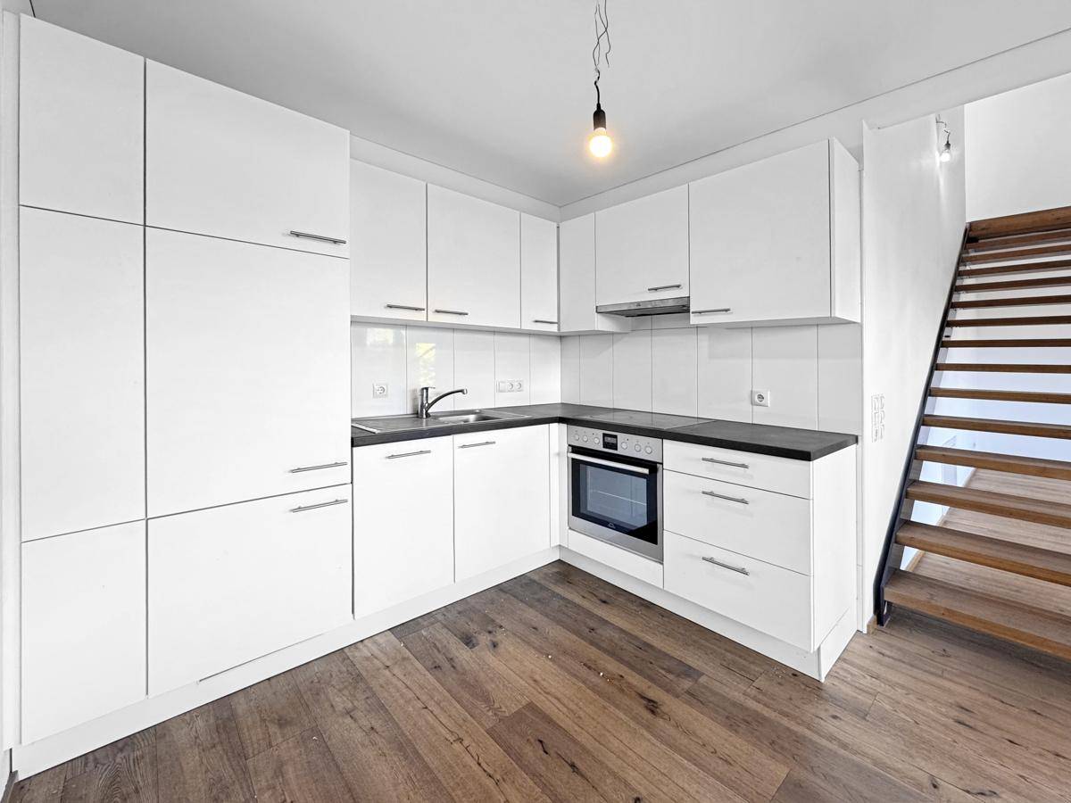Moderne Einbauküche mit weißen Schränken, dunkler Arbeitsplatte und Holzboden.