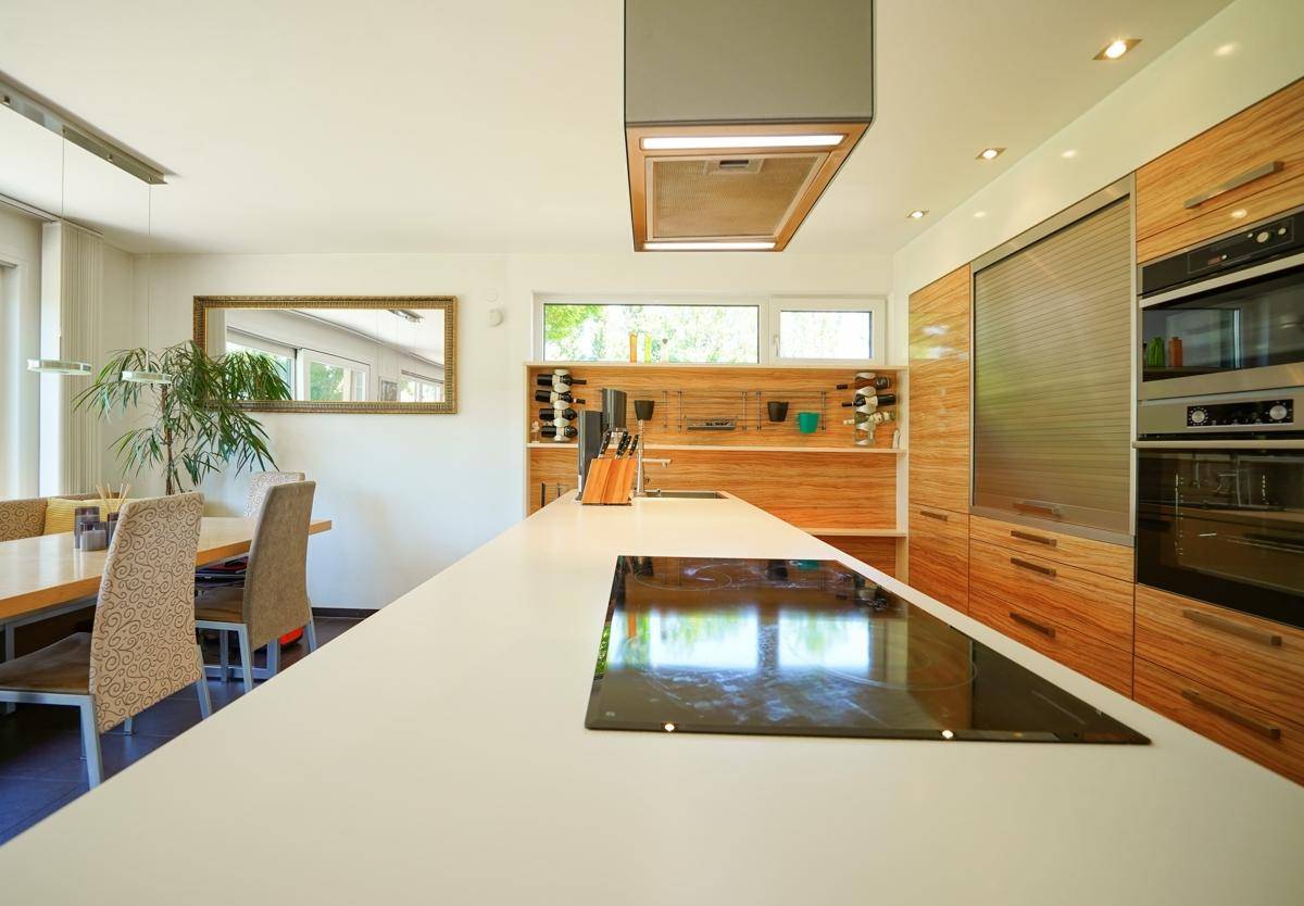 Moderne Küche mit Holzfronten, Kochinsel und integrierten Geräten, offen zum Essbereich.