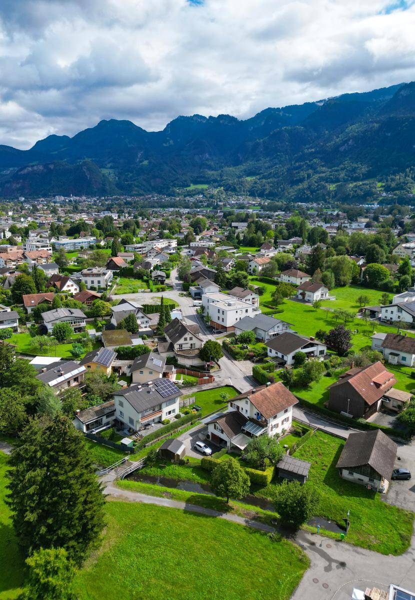 Umfassende Luftaufnahme der Gemeinde mit Wohngebieten und weitreichendem Blick auf die Alpen.