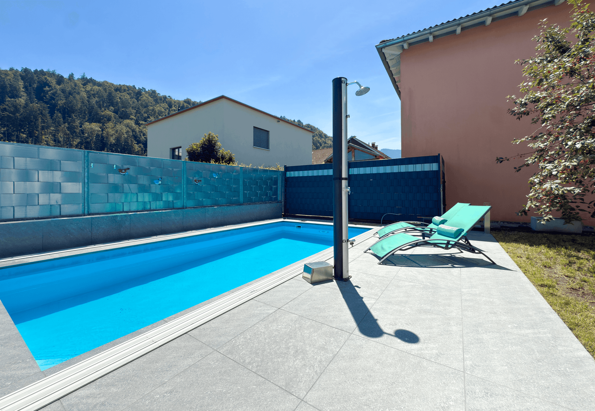 Privater Poolbereich mit Außendusche, Liegestühlen und Blick auf die Berge.