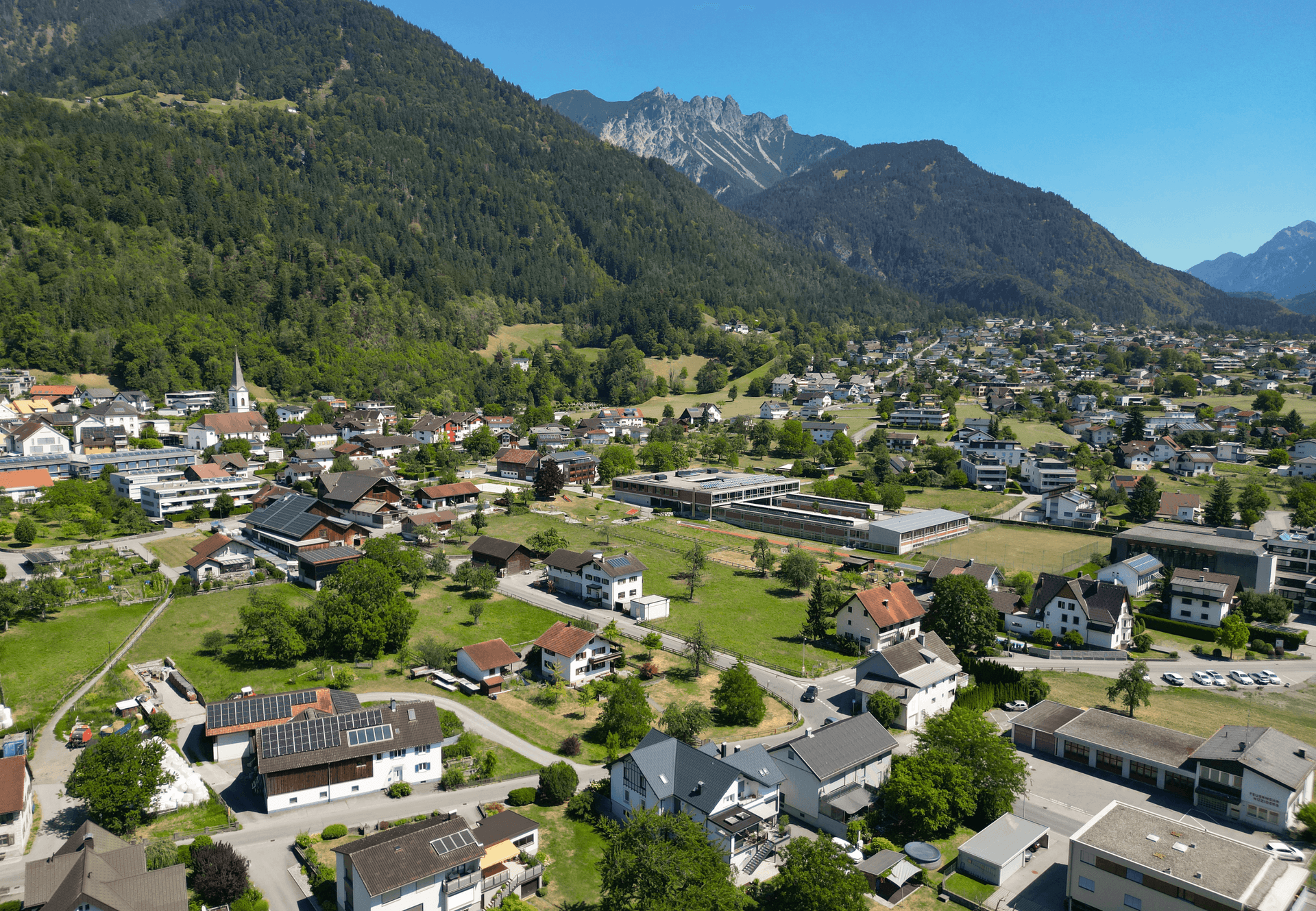 Panoramablick auf die Stadt Nüziders mit umliegenden Bergen und Wohngebieten.
