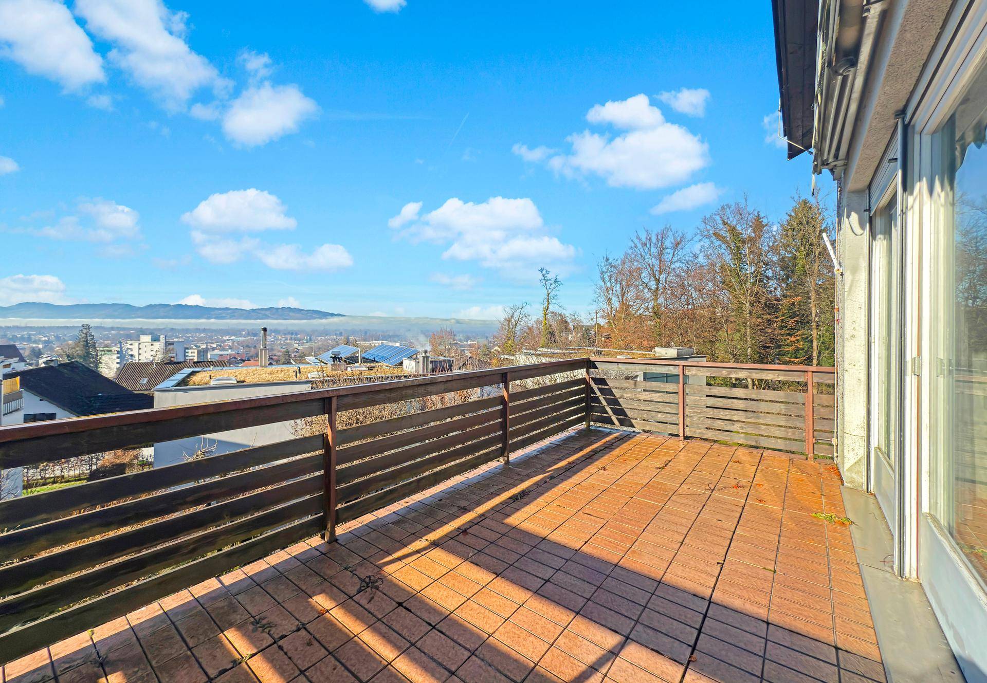 Großer Balkon mit Fliesenboden und weitem Blick über die Stadt und die Landschaft.