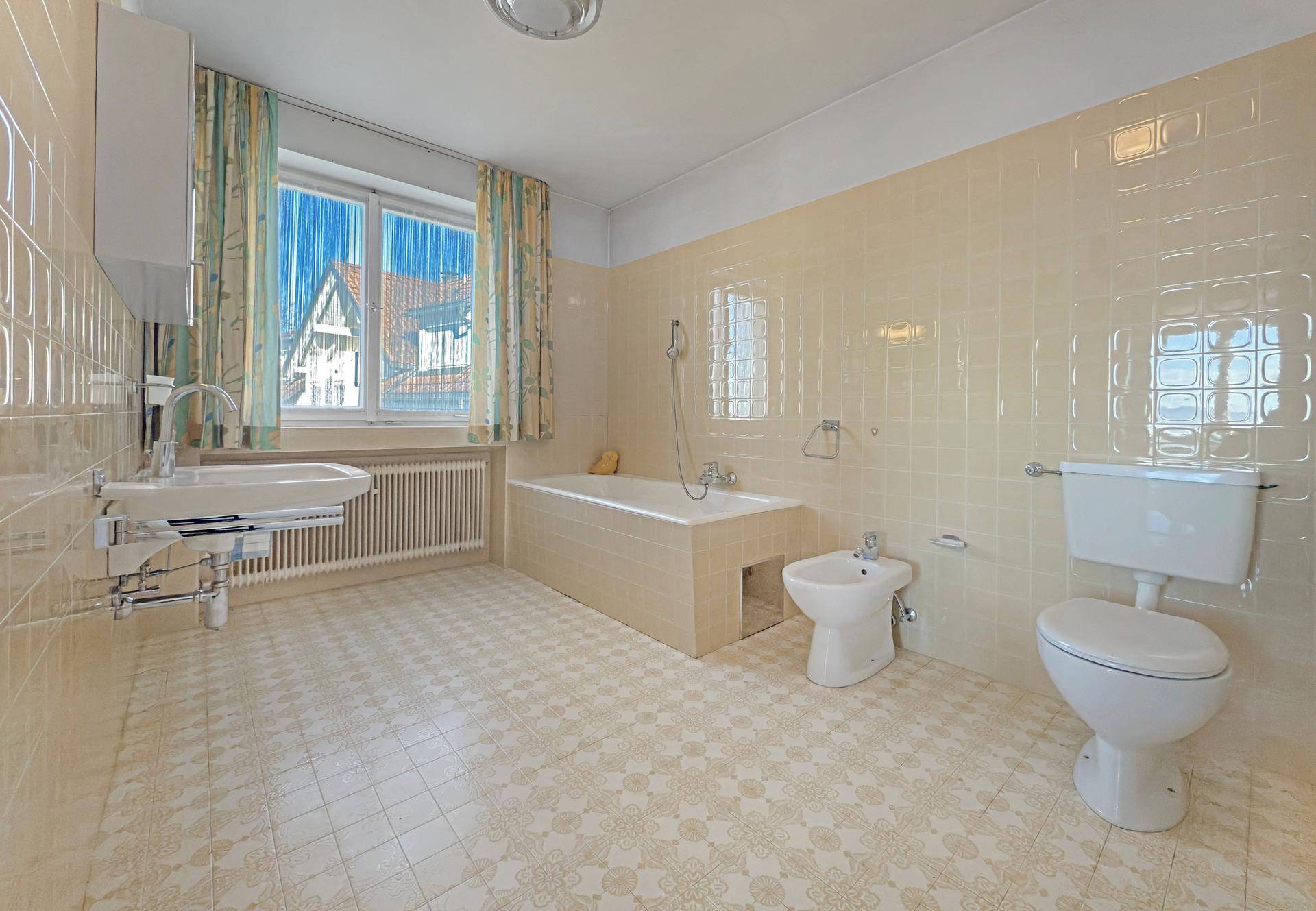 Geräumiges Badezimmer mit Badewanne, Bidet, WC und Fenster in einem älteren Stil.