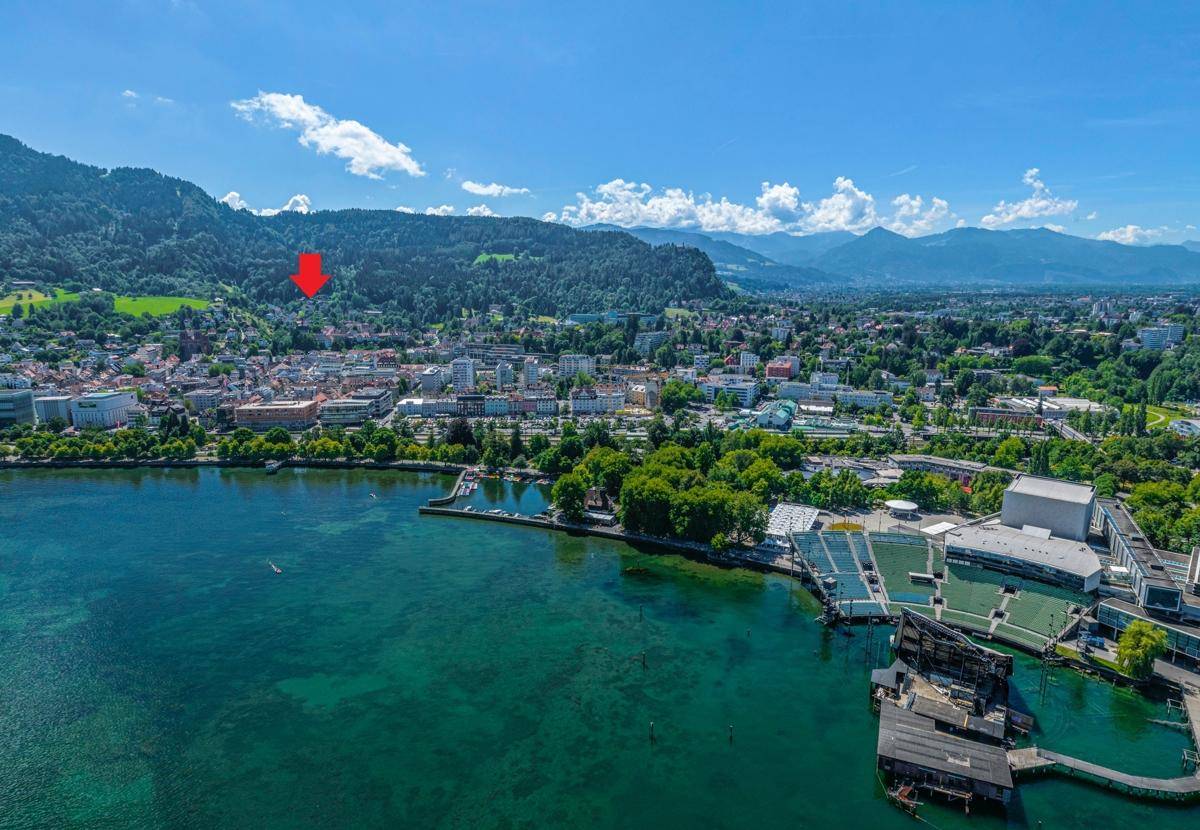 Luftaufnahme einer Küstenstadt am See mit Bergen im Hintergrund unter blauem Himmel.