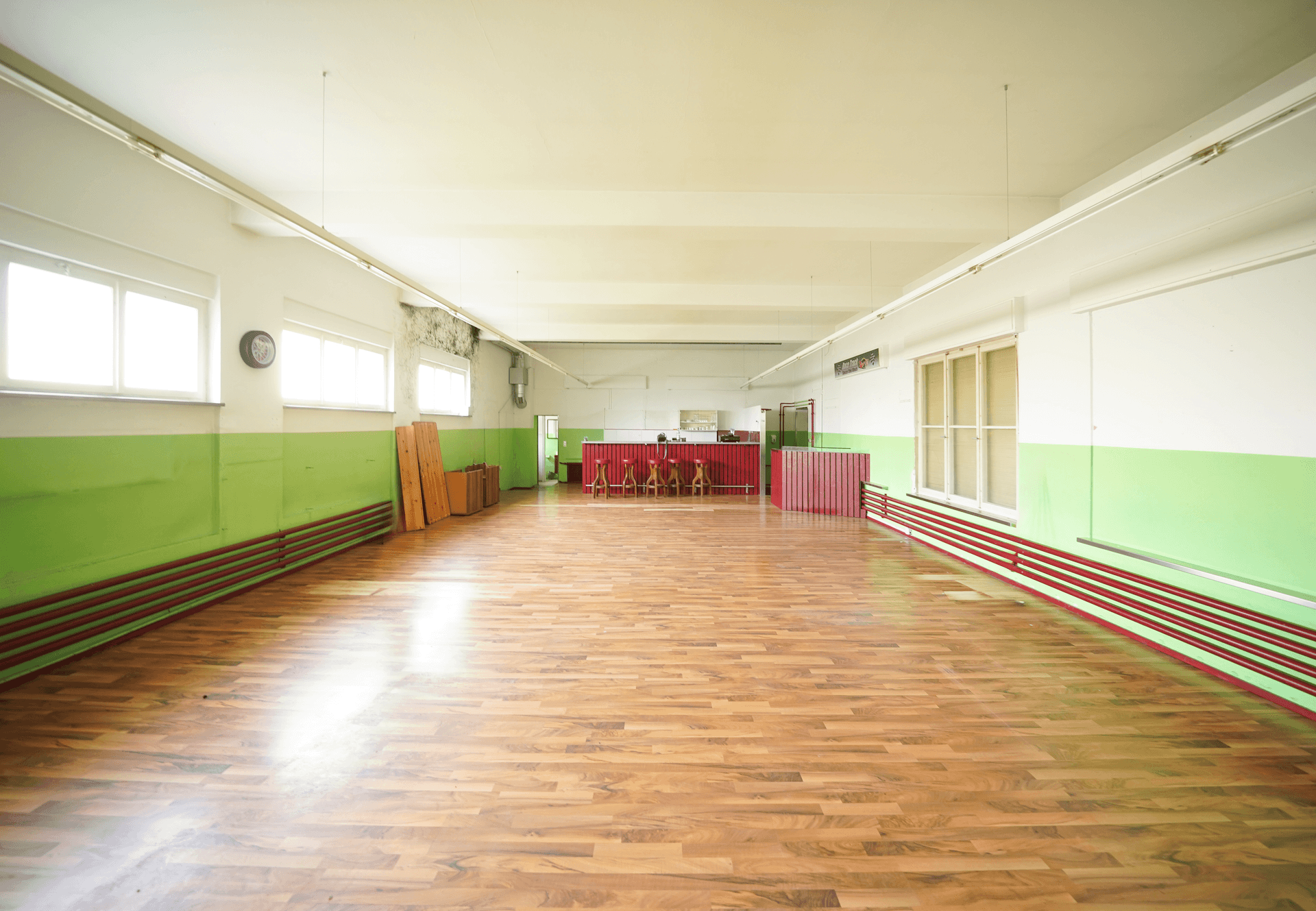 Großer Gemeinschaftsraum mit Holzboden, farbigen Wänden und einer Theke im Hintergrund.