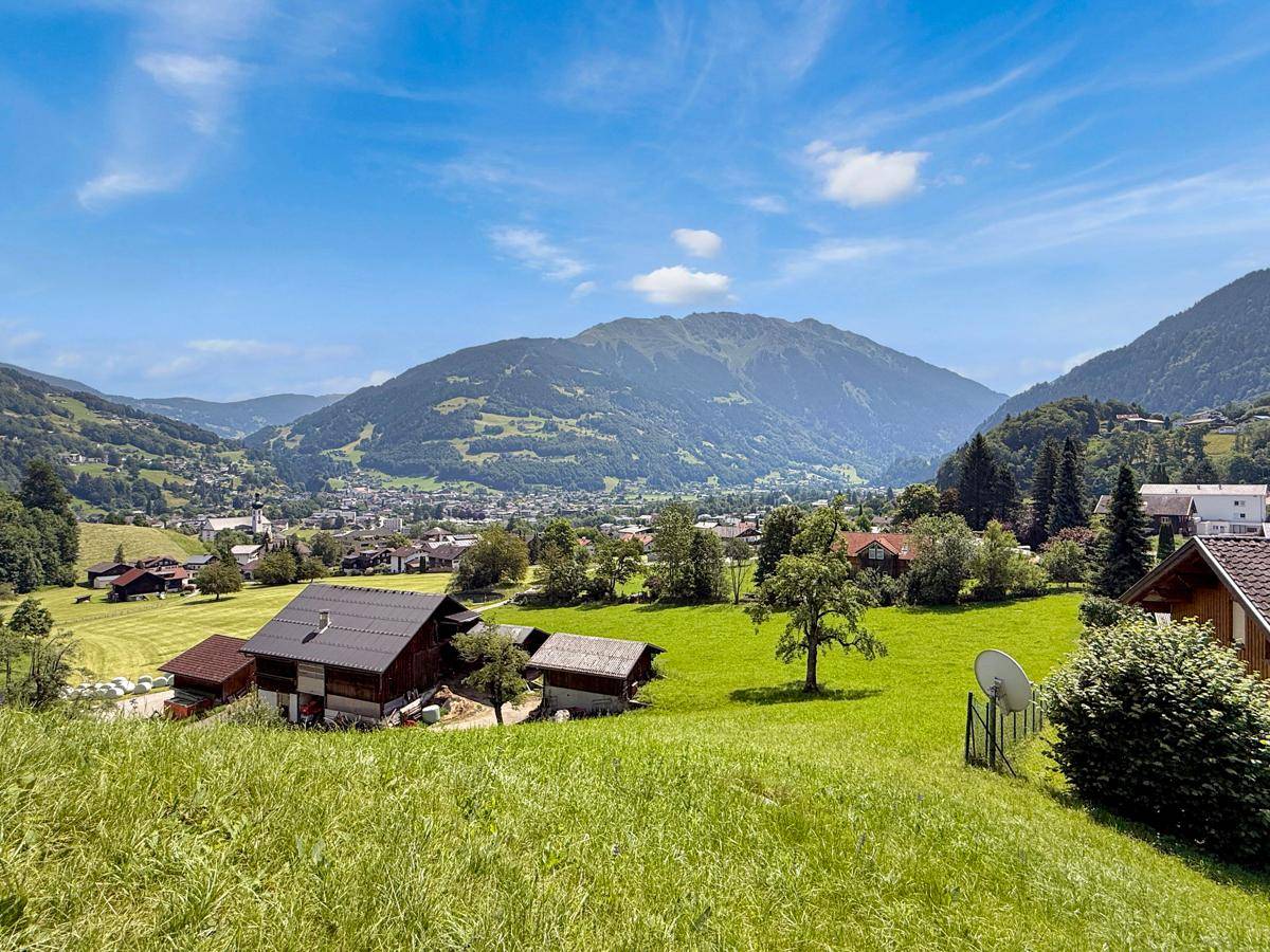 Blick über ein malerisches Dorf im Tal, umgeben von grünen Hügeln und hohen Bergen.