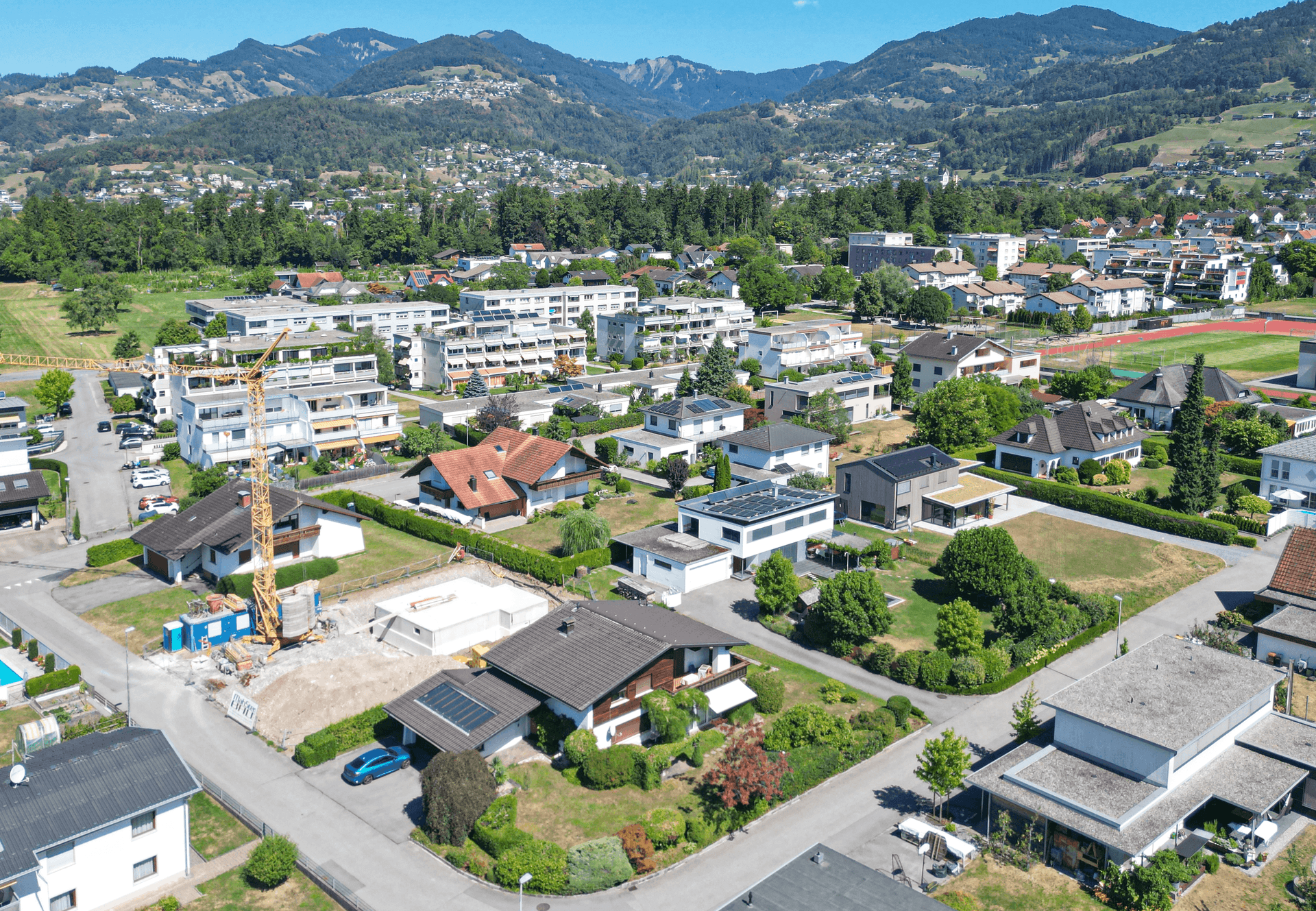 Weitläufige Luftaufnahme der Wohnsiedlung mit Einfamilienhäusern und Bergen im Hintergrund.