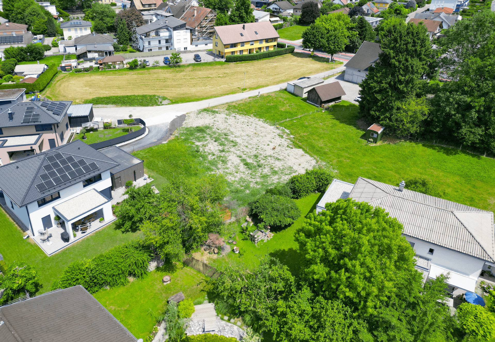 Weitläufige Luftaufnahme eines Baugrundstücks in einer grünen Wohngegend mit Bergblick.