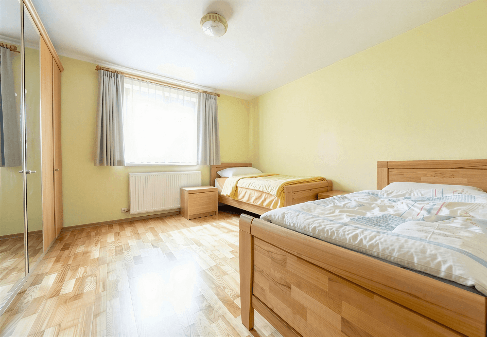 Helles Schlafzimmer mit zwei Einzelbetten, Parkettboden und großem Fenster.