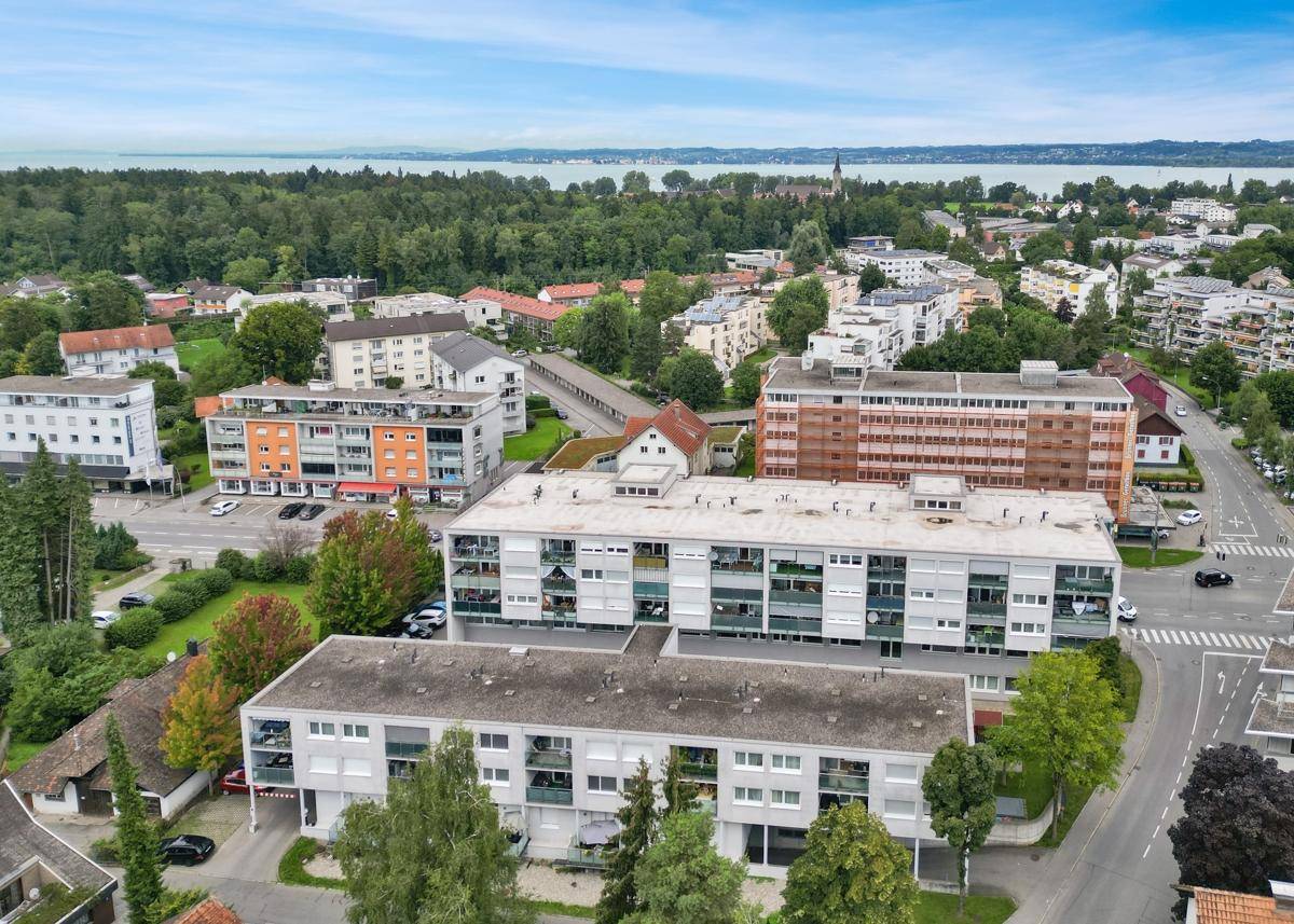 Luftaufnahme einer Wohnsiedlung mit Gebäuden, Bäumen und einem See im Hintergrund.