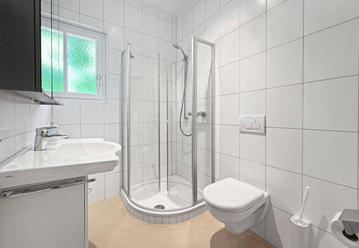 Modernes Badezimmer mit Duschkabine, wandhängendem WC und Fenster.