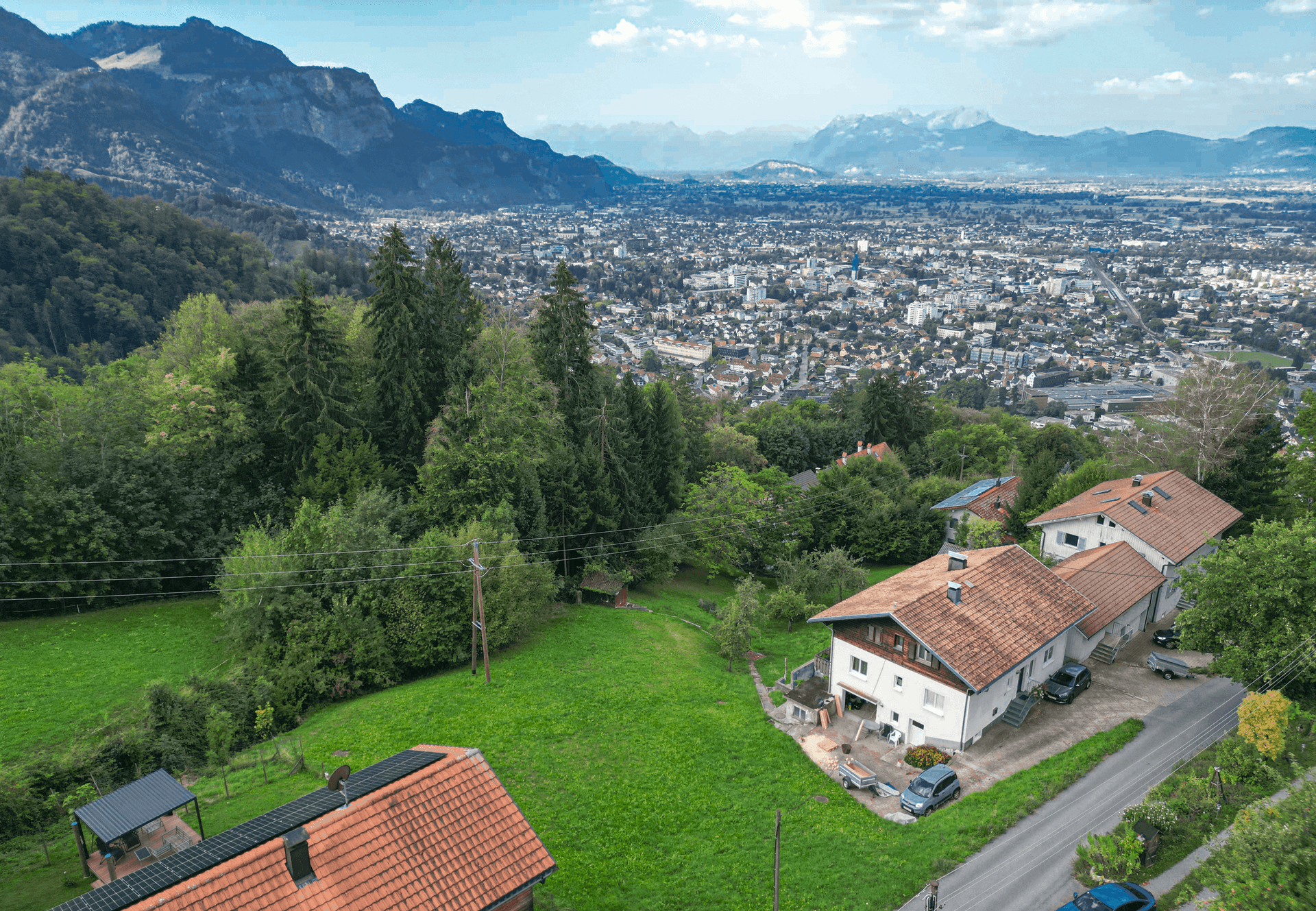Weitwinkelaufnahme von Häusern, grünen Flächen und einer ausgedehnten Stadtansicht mit Bergpanorama.