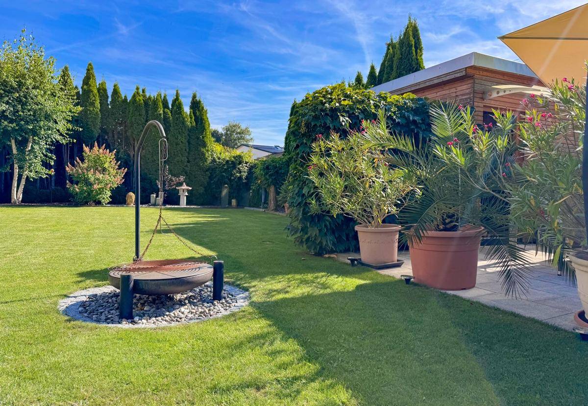 Gepflegter Gartenbereich mit Feuerstelle, üppigen Pflanzen und Rasenfläche.