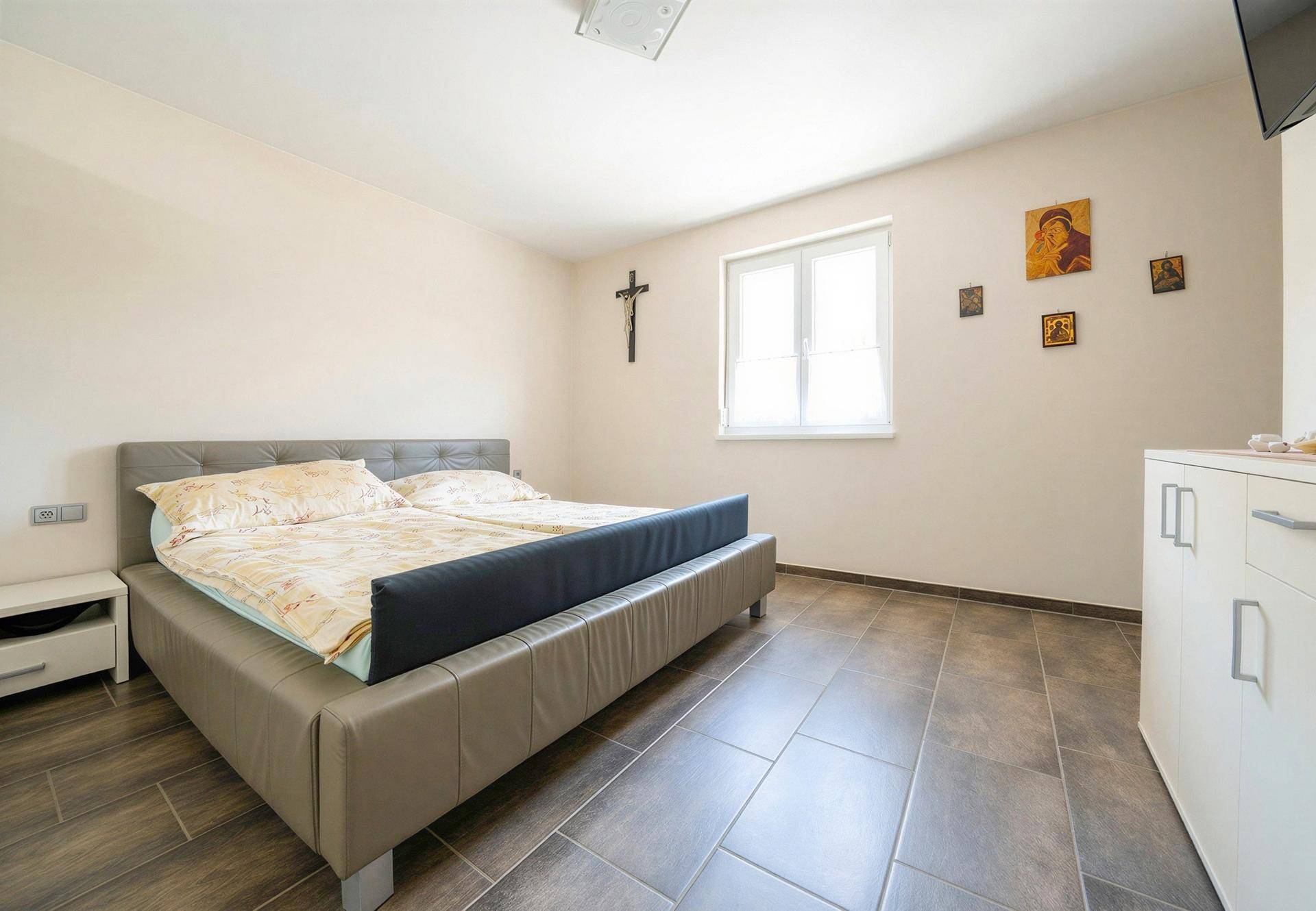 Schlafzimmer mit Doppelbett, Fliesenboden und Fenster für natürliches Licht.