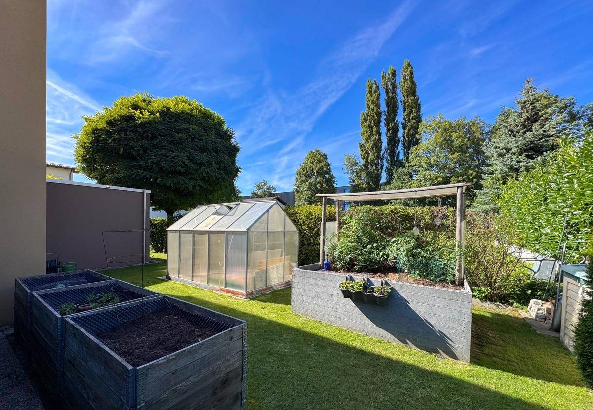 Funktionaler Gartenbereich mit Hochbeeten und einem Gewächshaus für den Anbau.