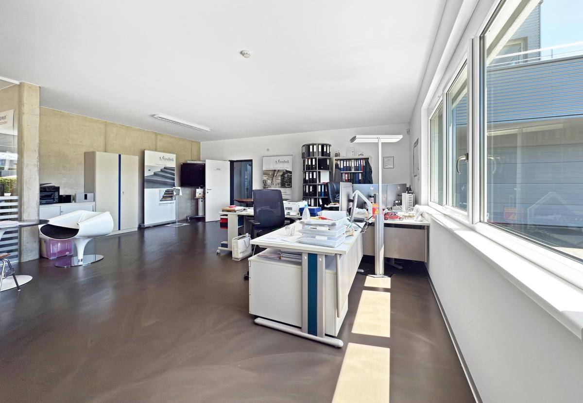 Helles und geräumiges Büro mit großen Fenstern, modernen Möbeln und glänzendem Boden.