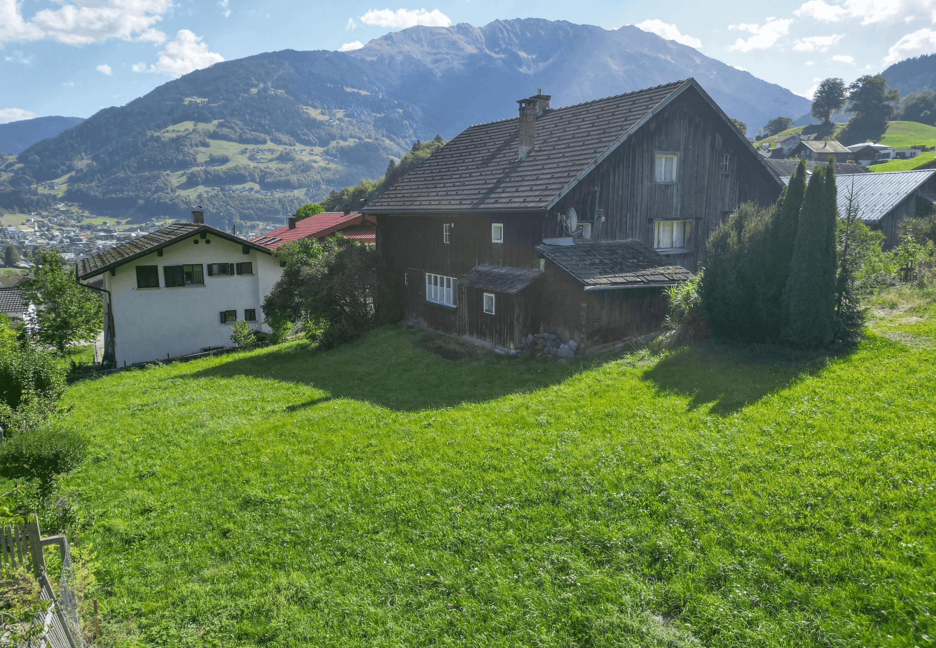 Rückansicht des Hauses mit großer Rasenfläche und Blick auf die umliegenden Berge und grüne Landschaft.