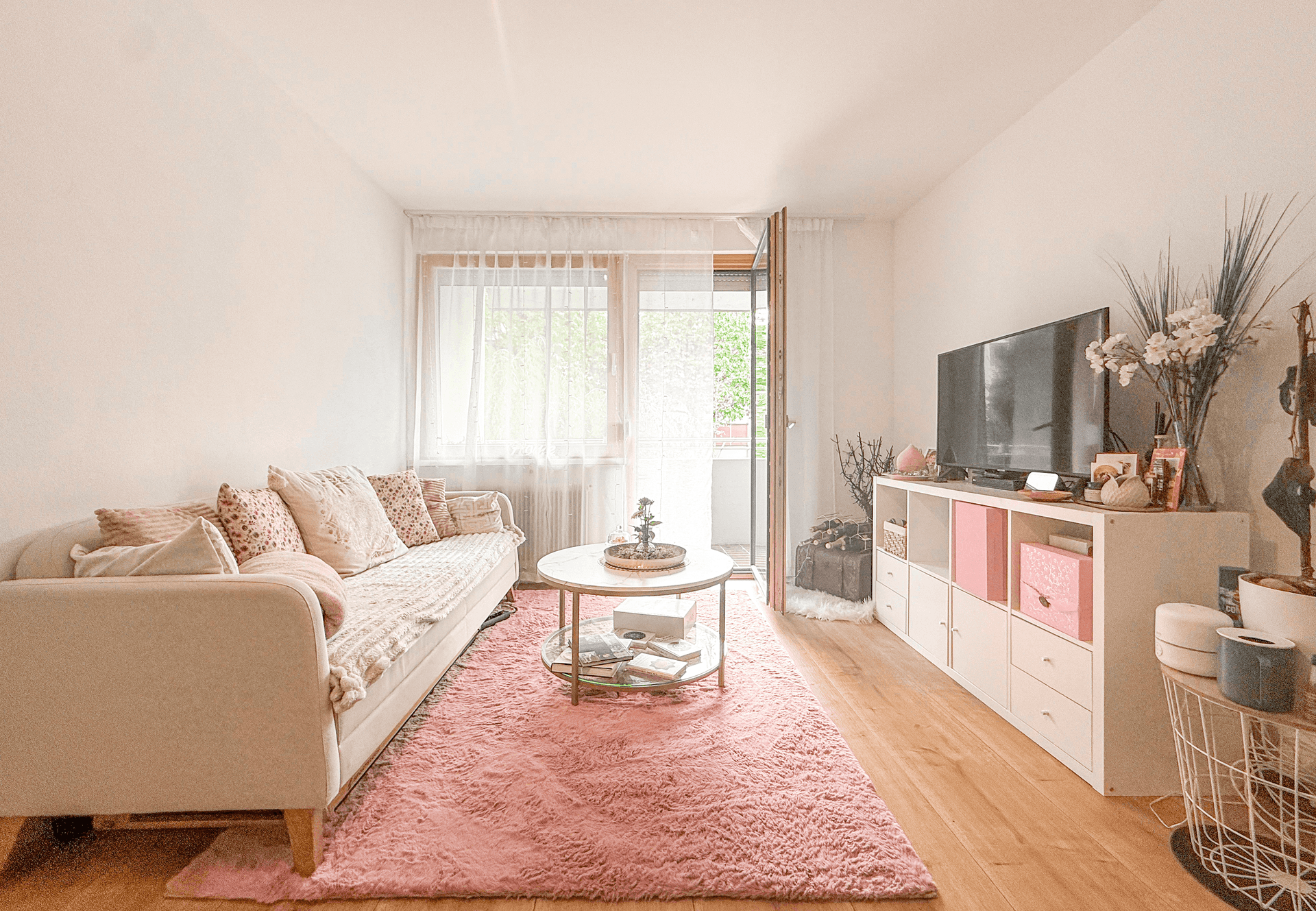 Gemütliches Wohnzimmer mit Sofa, rosa Teppich und Fernseher, hell und modern eingerichtet.