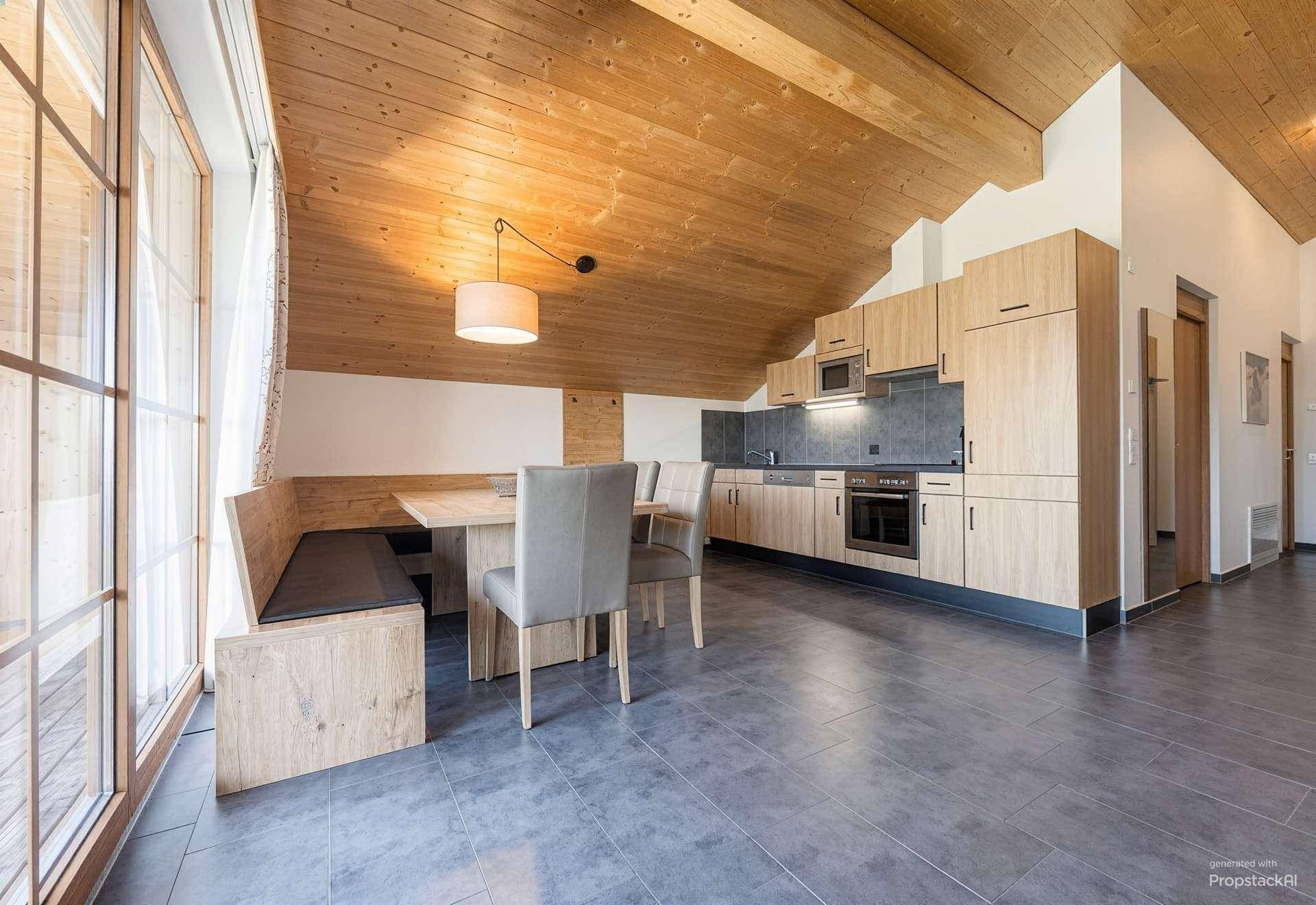Offener Wohn- und Essbereich mit moderner Holzküche, Holzbalkendecke und großformatigen Fliesenboden.