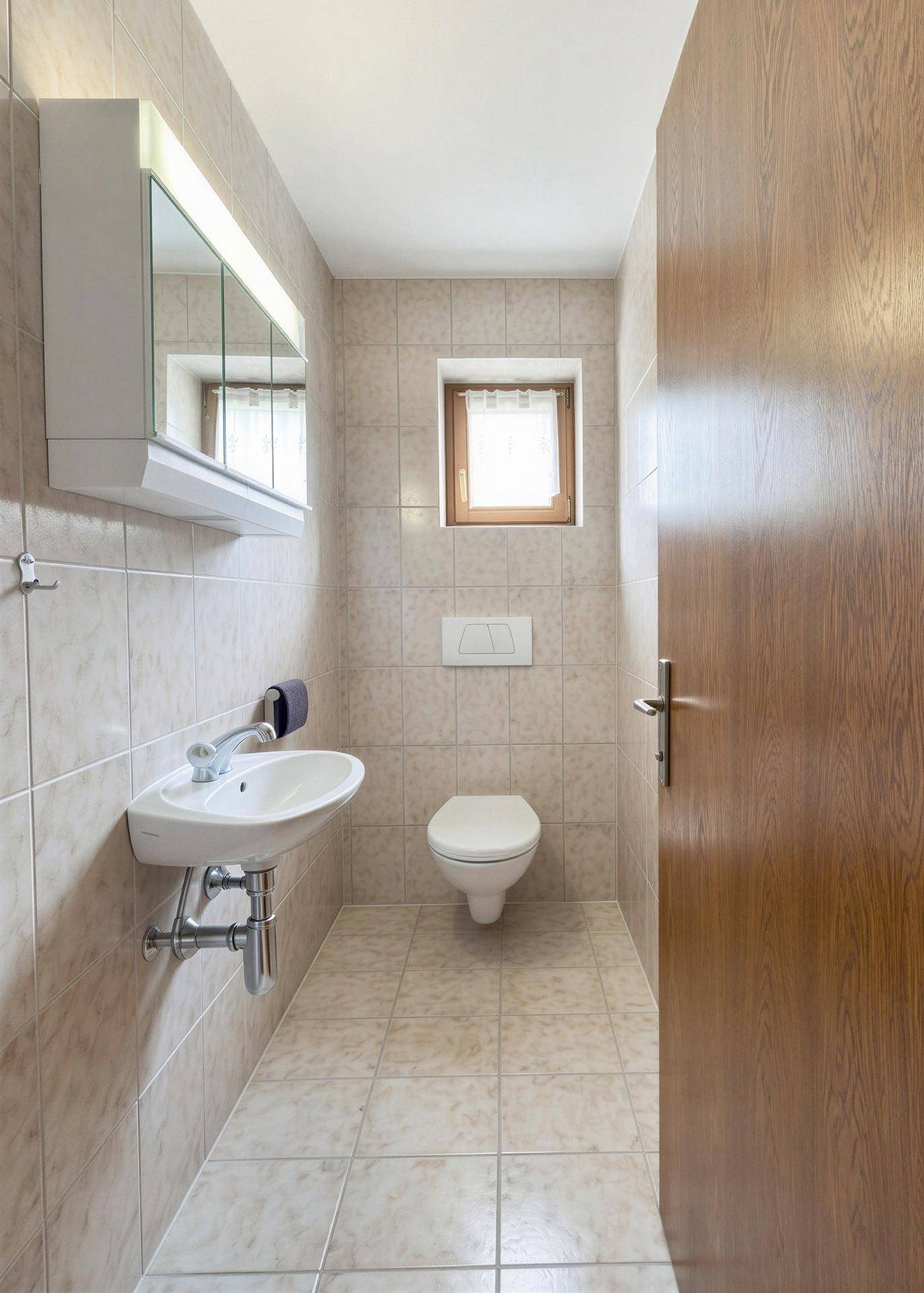 Kleines Gäste-WC mit Waschbecken, Spiegelschrank und Fenster.