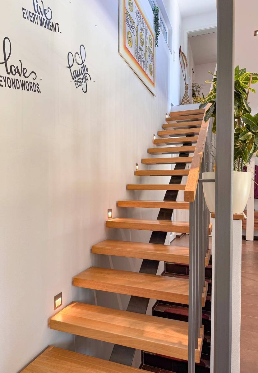Moderne Holztreppe mit indirekter Beleuchtung und dekorativen Wandaufklebern.