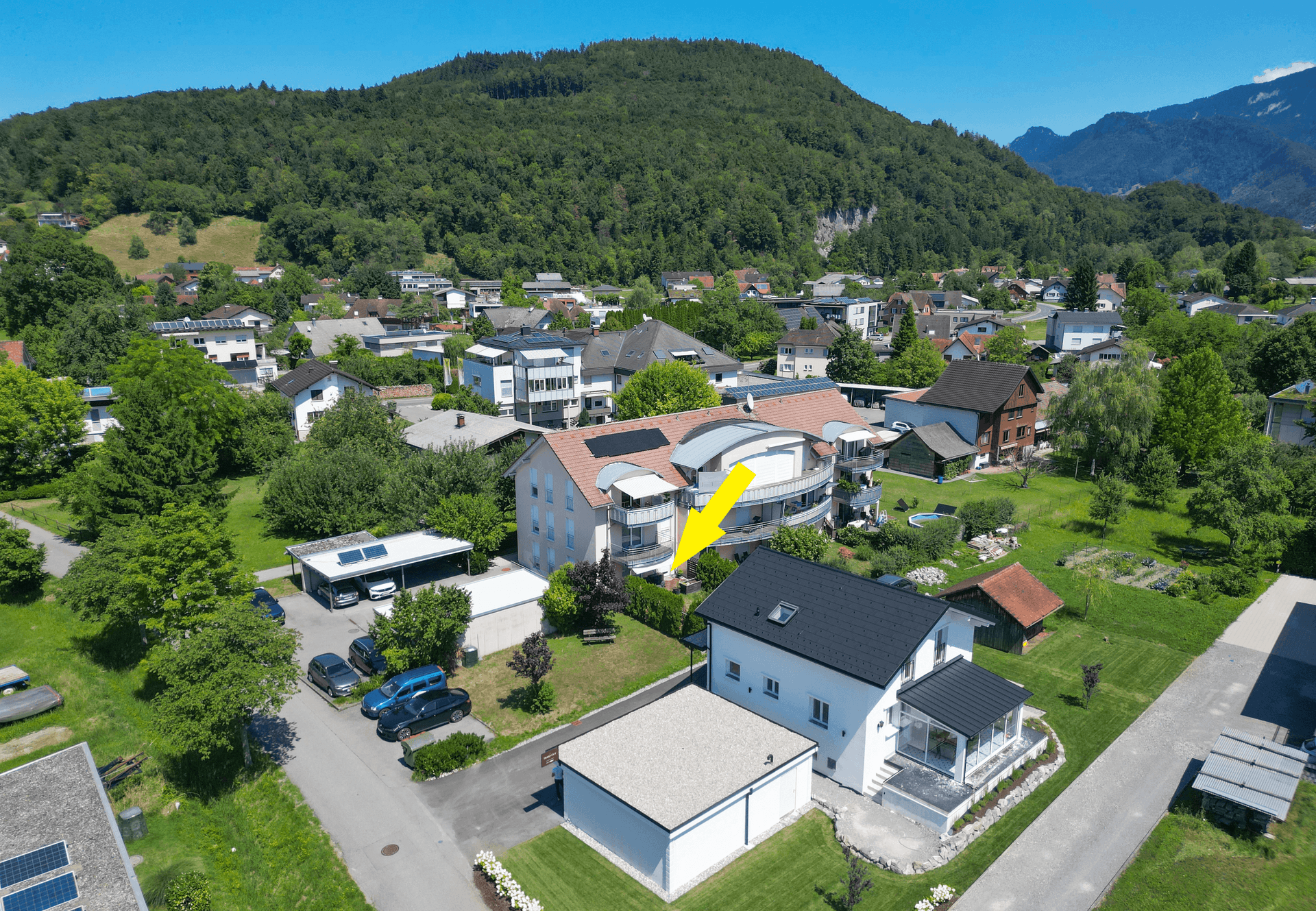 Luftaufnahme der Wohnsiedlung mit markiertem Gebäude, umgeben von Natur und Bergen.