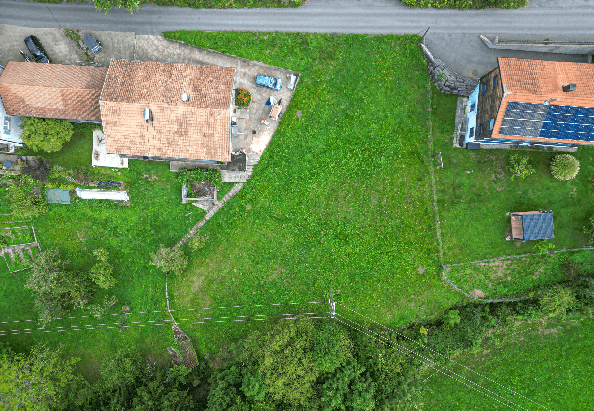 Senkrechte Luftaufnahme eines Hauses mit Terrasse, einer grünen Parzelle und einem weiteren Haus mit Solaranlage.