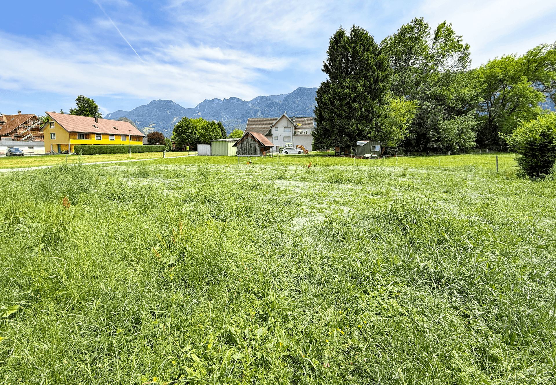 Weitläufiges grünes Grundstück mit Blick auf die umliegende Berglandschaft und vereinzelte Häuser.
