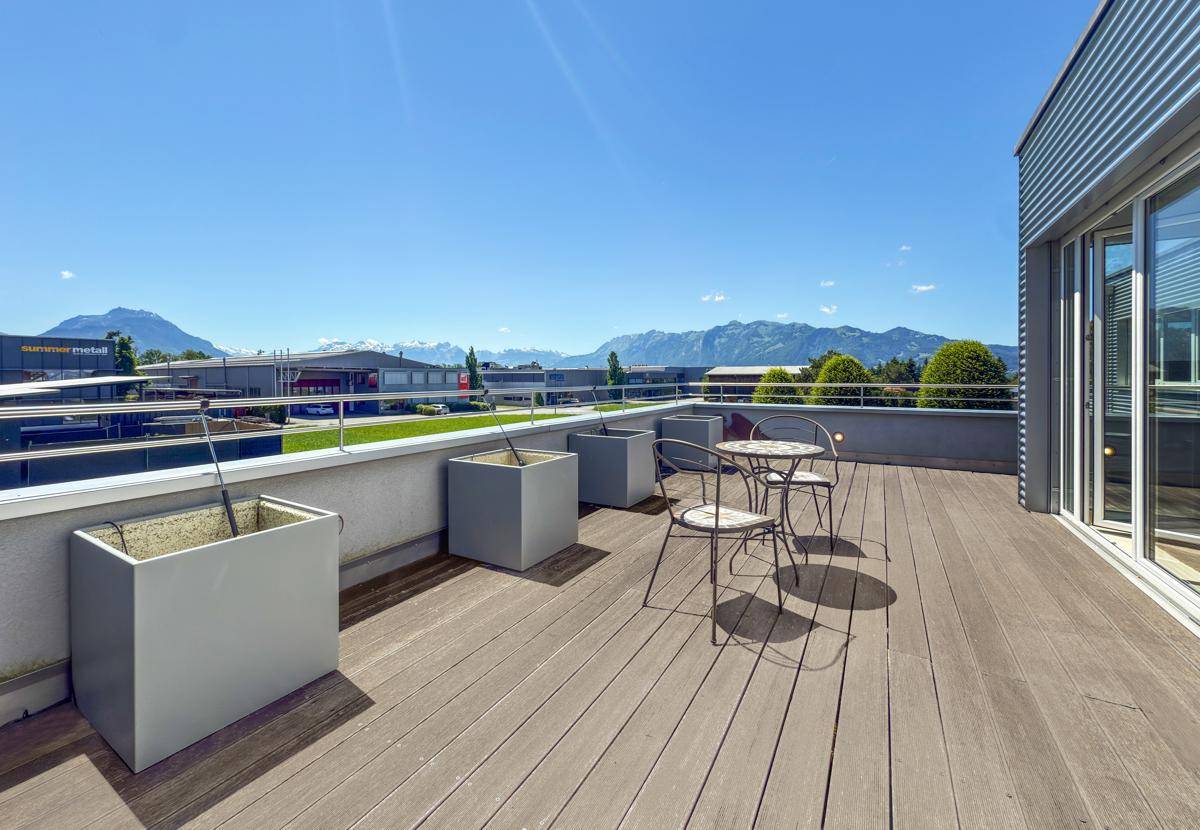 Sonnige Dachterrasse mit Holzbelag, Metalltisch, Stühlen und einem Panoramablick auf die Berge.