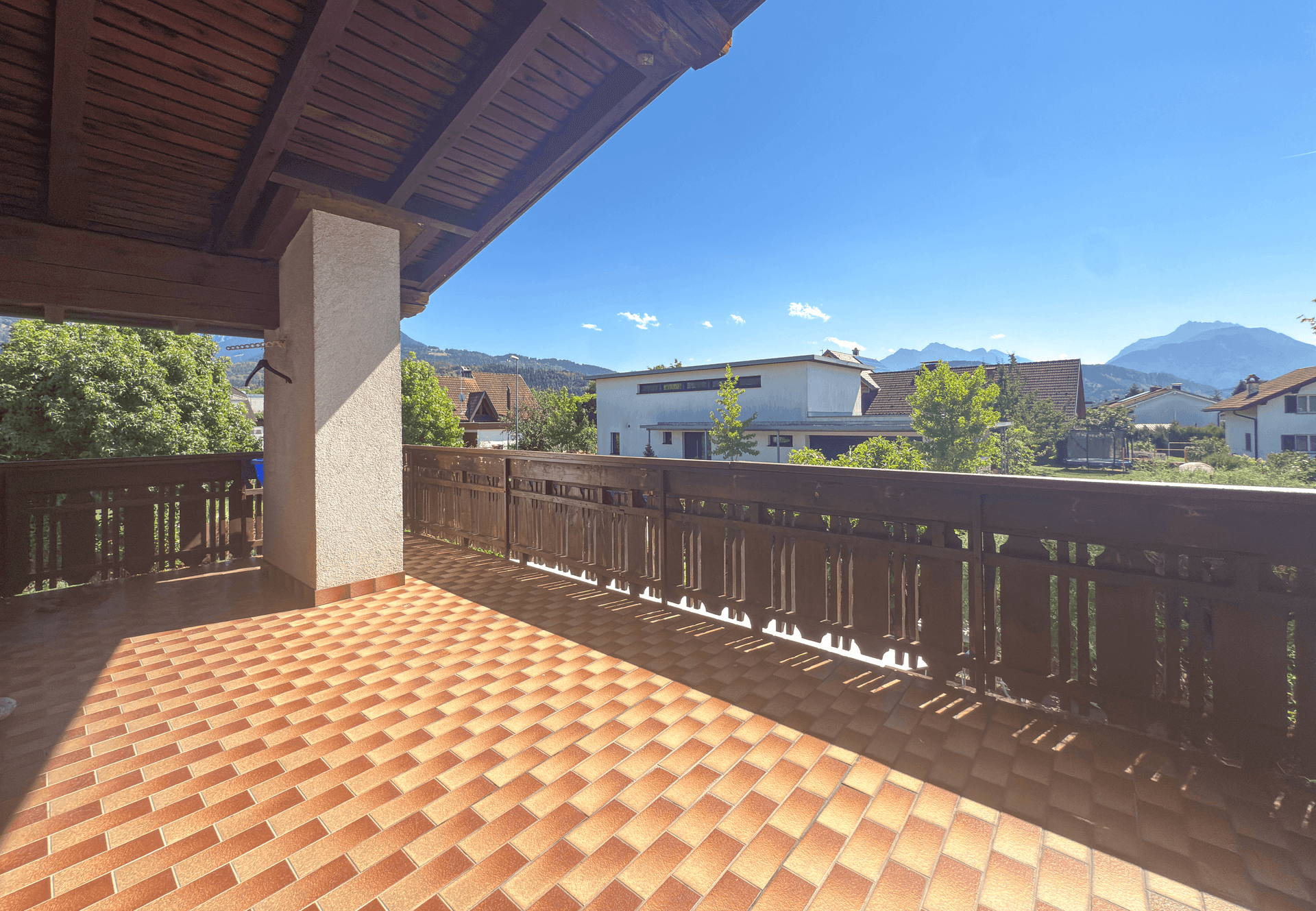 Geräumiger Balkon mit Fliesenboden, Holzgeländer und weitem Bergblick.
