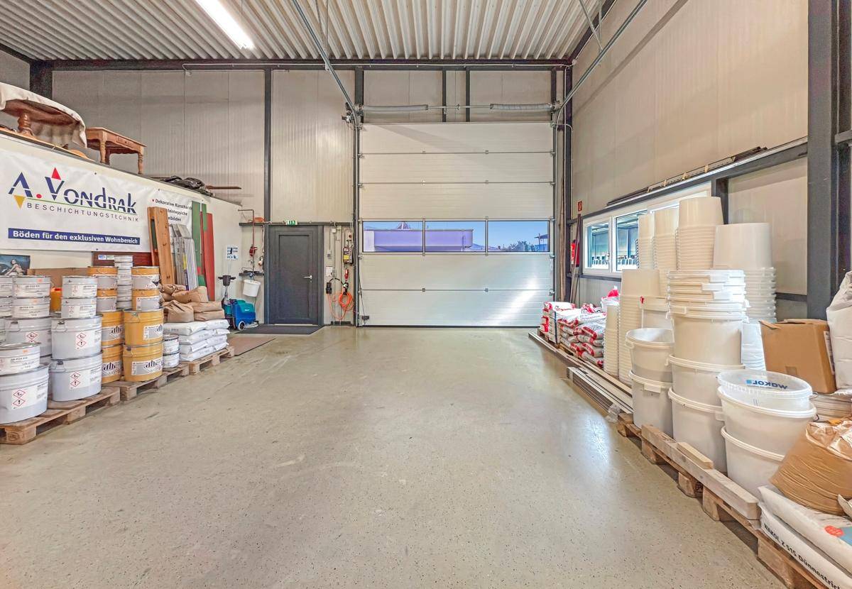 Lagerhalle mit einem großen Rolltor, hohen Decken und gestapelten Eimern und Säcken.