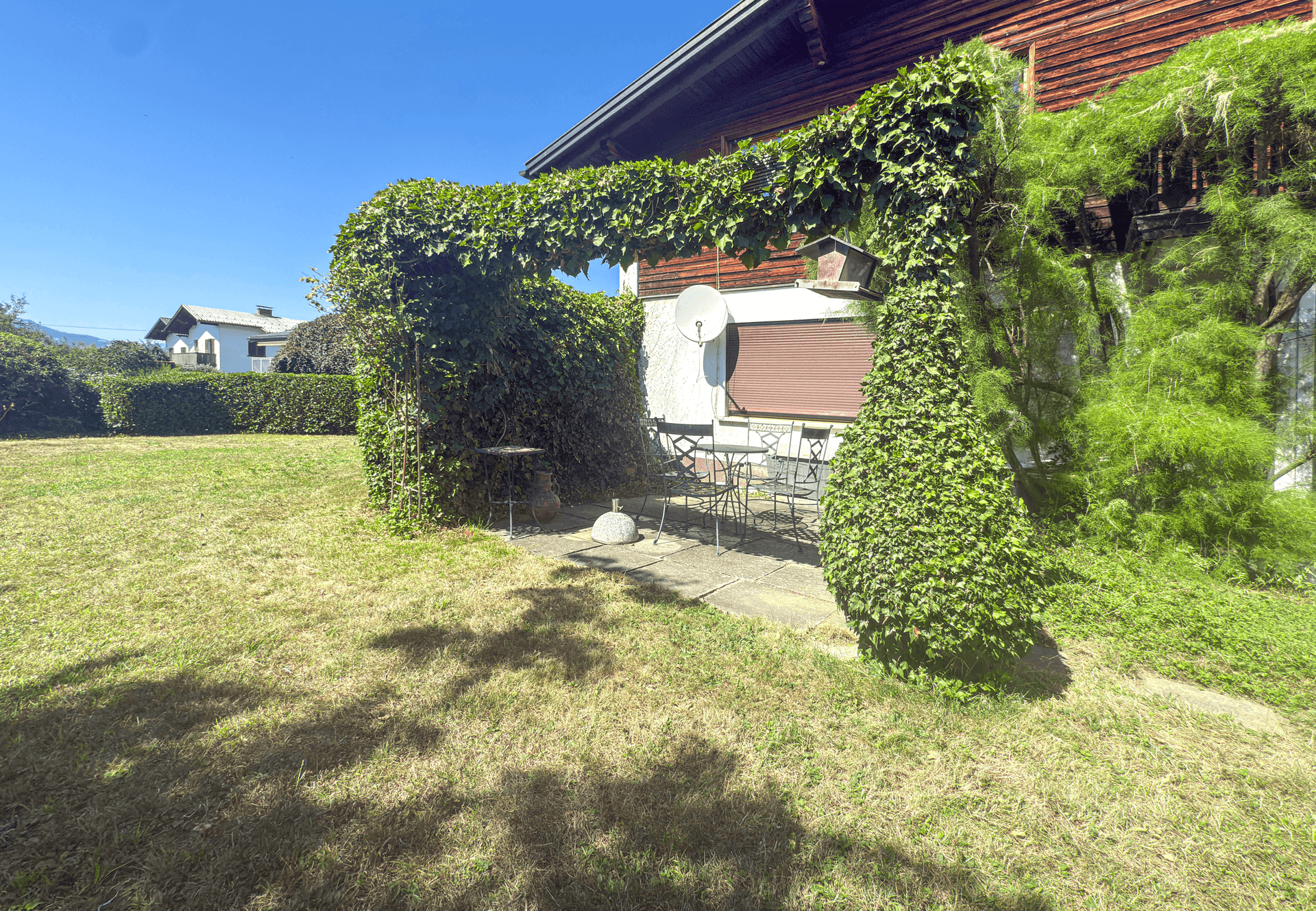 Gepflegter Gartenbereich mit Rasenfläche, Sitzgelegenheit und üppiger Bepflanzung.