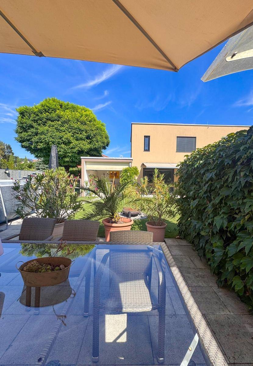 Gemütlicher Terrassenbereich mit Glasstisch und Stühlen, umgeben von Grün.