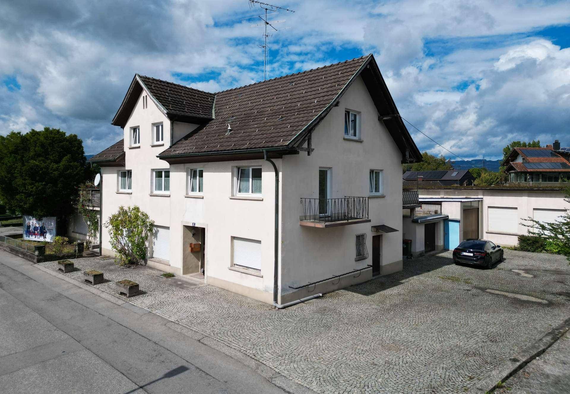Vorder- und Seitenansicht des Hauses mit einem kleinen Balkon und gepflastertem Vorplatz.