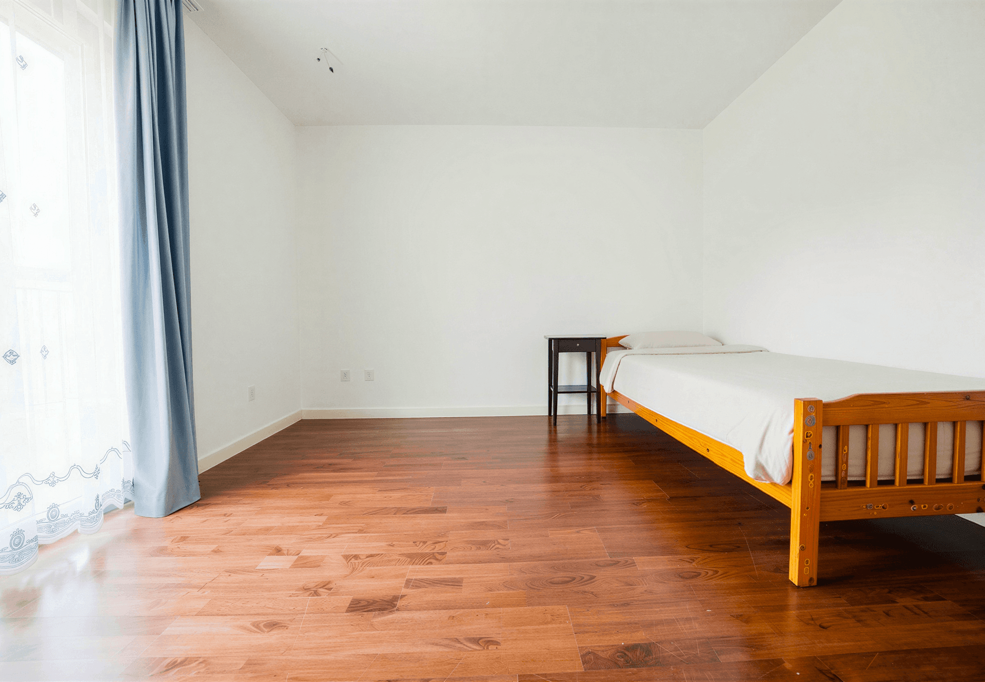 Helles Schlafzimmer mit Holzboden, Einzelbett und großem Fenster mit blauen Vorhängen, sehr ruhig gelegen.