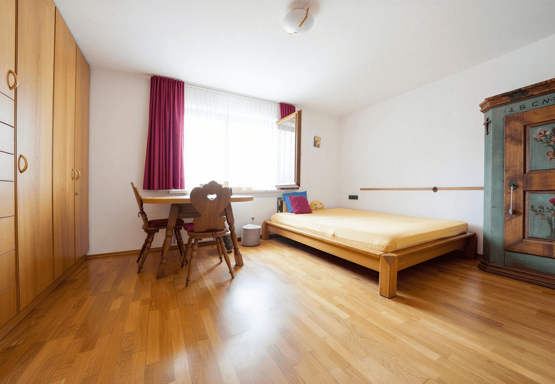 Helles Schlafzimmer mit Holzboden, Einzelbett und traditionellem bemalten Schrank.