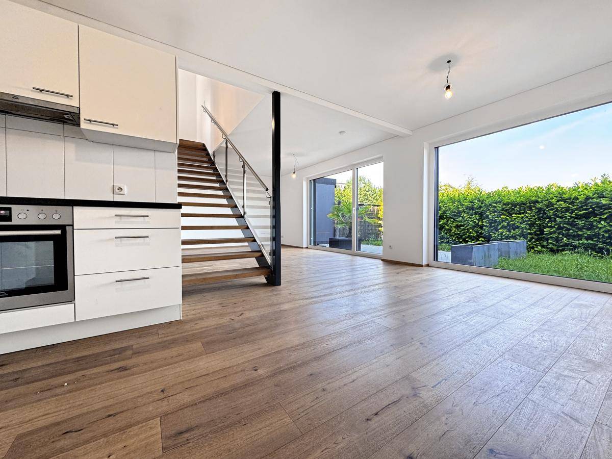 Offener Wohnbereich mit Holzboden, Treppe und großen Fenstern zum Garten.