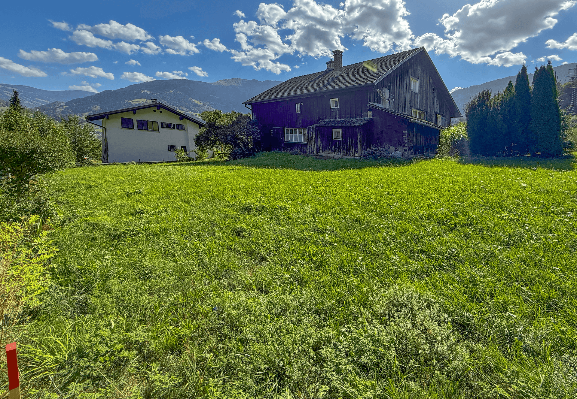 Weitläufige Rasenfläche hinter dem Haus mit Blick auf die Berge und den blauen Himmel an einem sonnigen Tag.