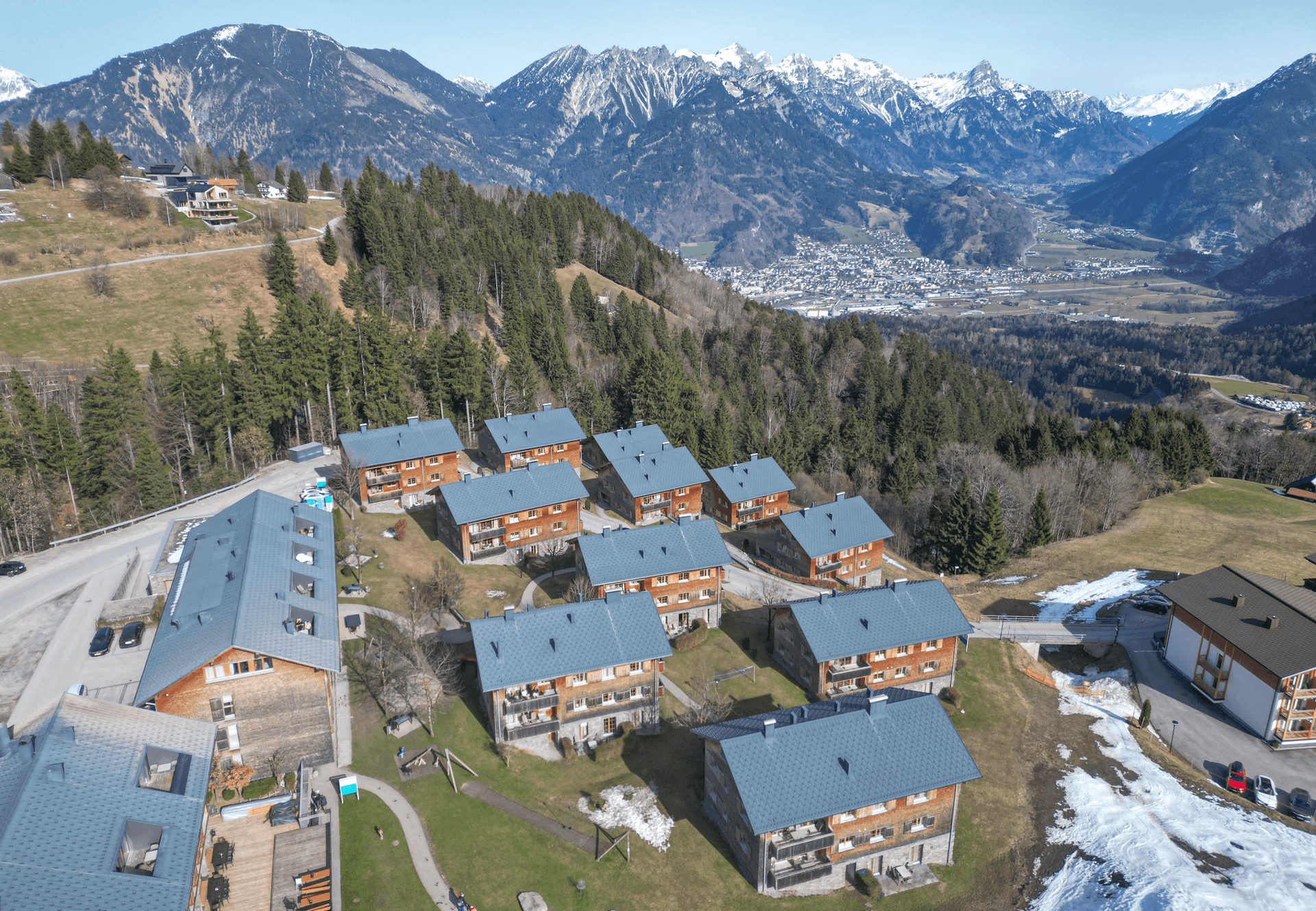 Luftaufnahme einer Wohnanlage in alpiner Landschaft mit vielen Gebäuden und Bergblick.