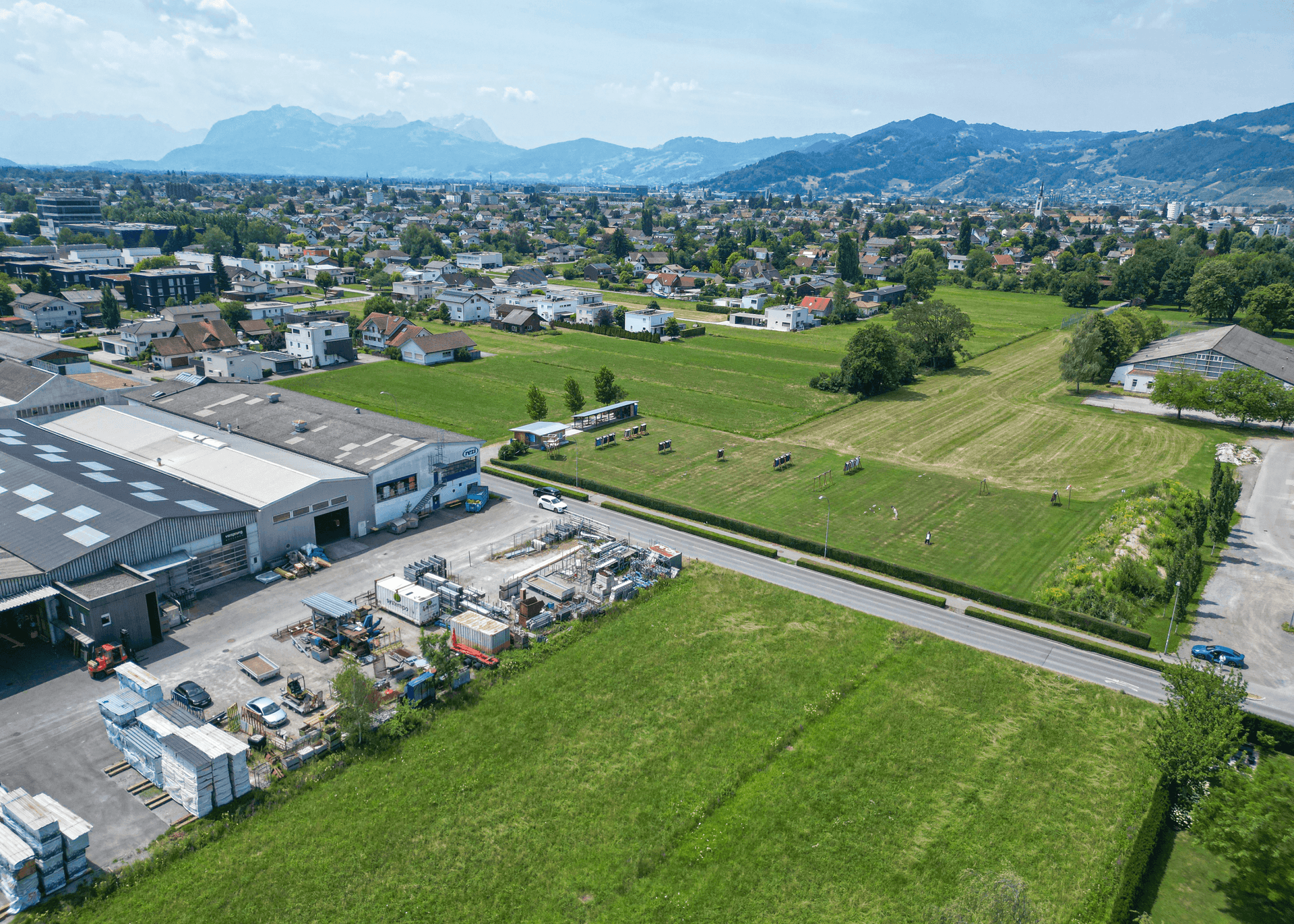 Panoramische Luftaufnahme einer Stadtlandschaft mit Feldern, Industriegebieten und einer beeindruckenden Bergkulisse.