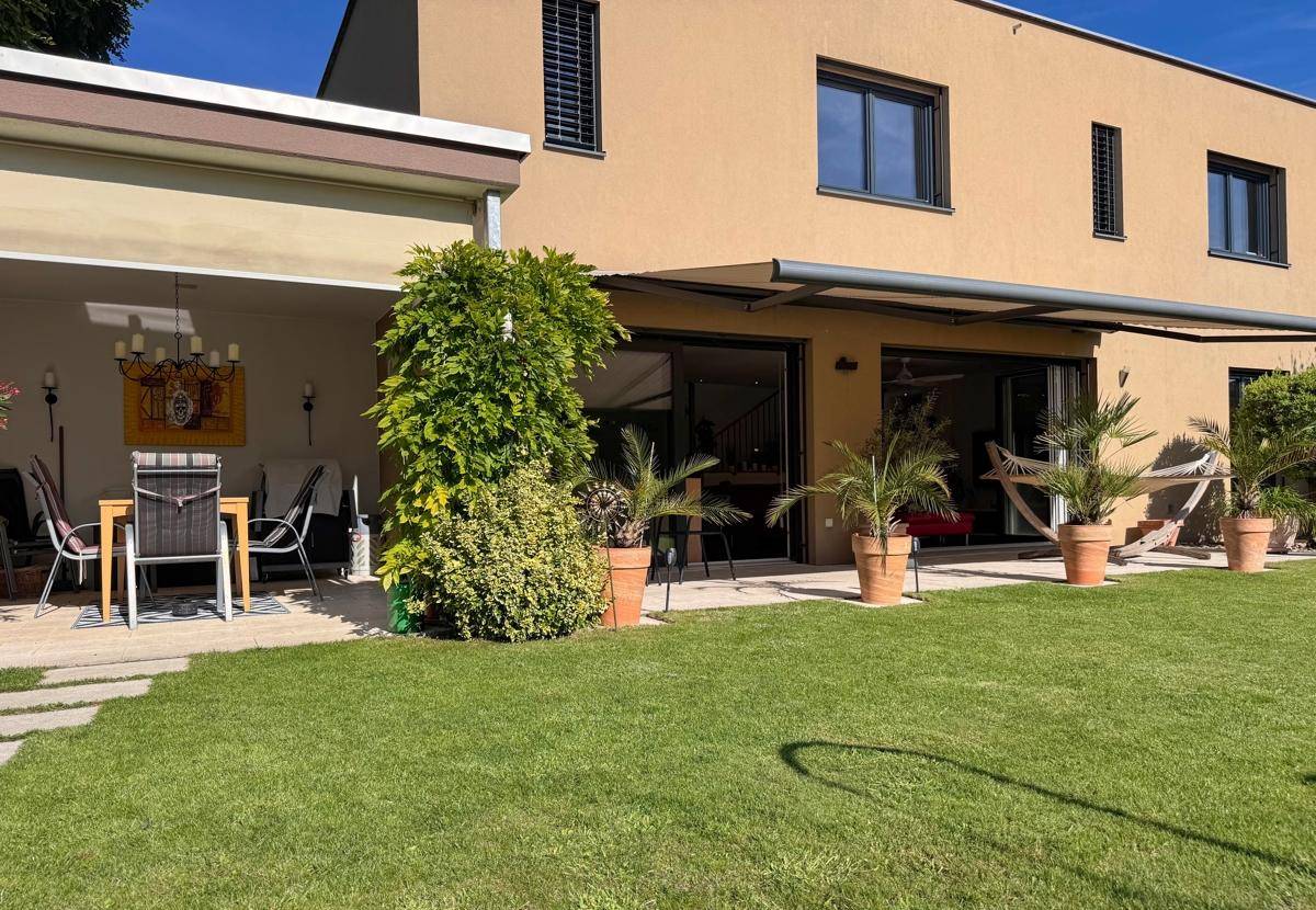 Moderner Hausanbau mit großer Rasenfläche und verschiedenen Pflanzen im Garten.