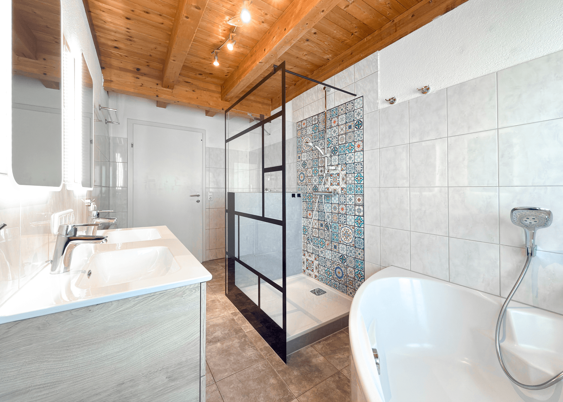 Modernes Badezimmer mit freistehender Badewanne, großer Dusche mit gemusterten Fliesen und Doppelwaschbecken unter Holzbalkendecke.